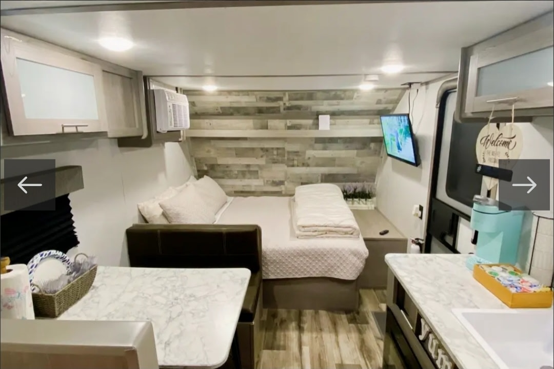 Modern rv rental interior with a cozy bed, dinette, kitchenette, TV, and wood-paneled wall. Ideal for your next adventure.. Dutchmen Coleman Lantern LT 2022