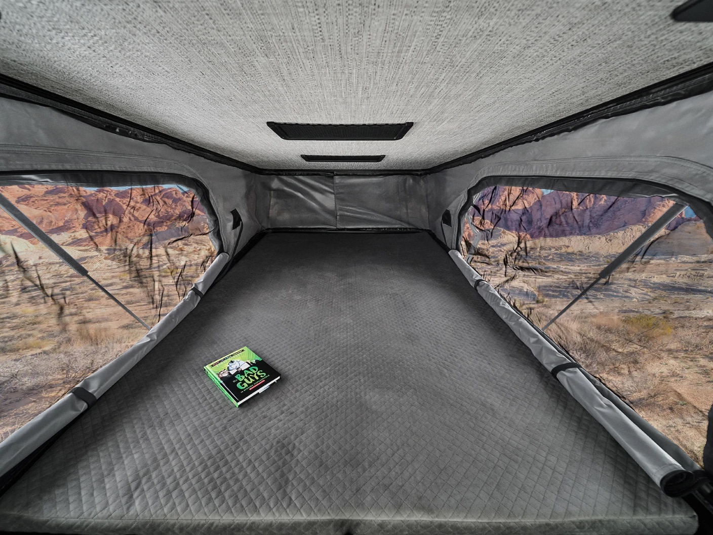 RV rental pop-up tent interior: quilted mattress, scenic desert views, and a book. Your cozy adventure awaits.. Winnebago Solis 2023