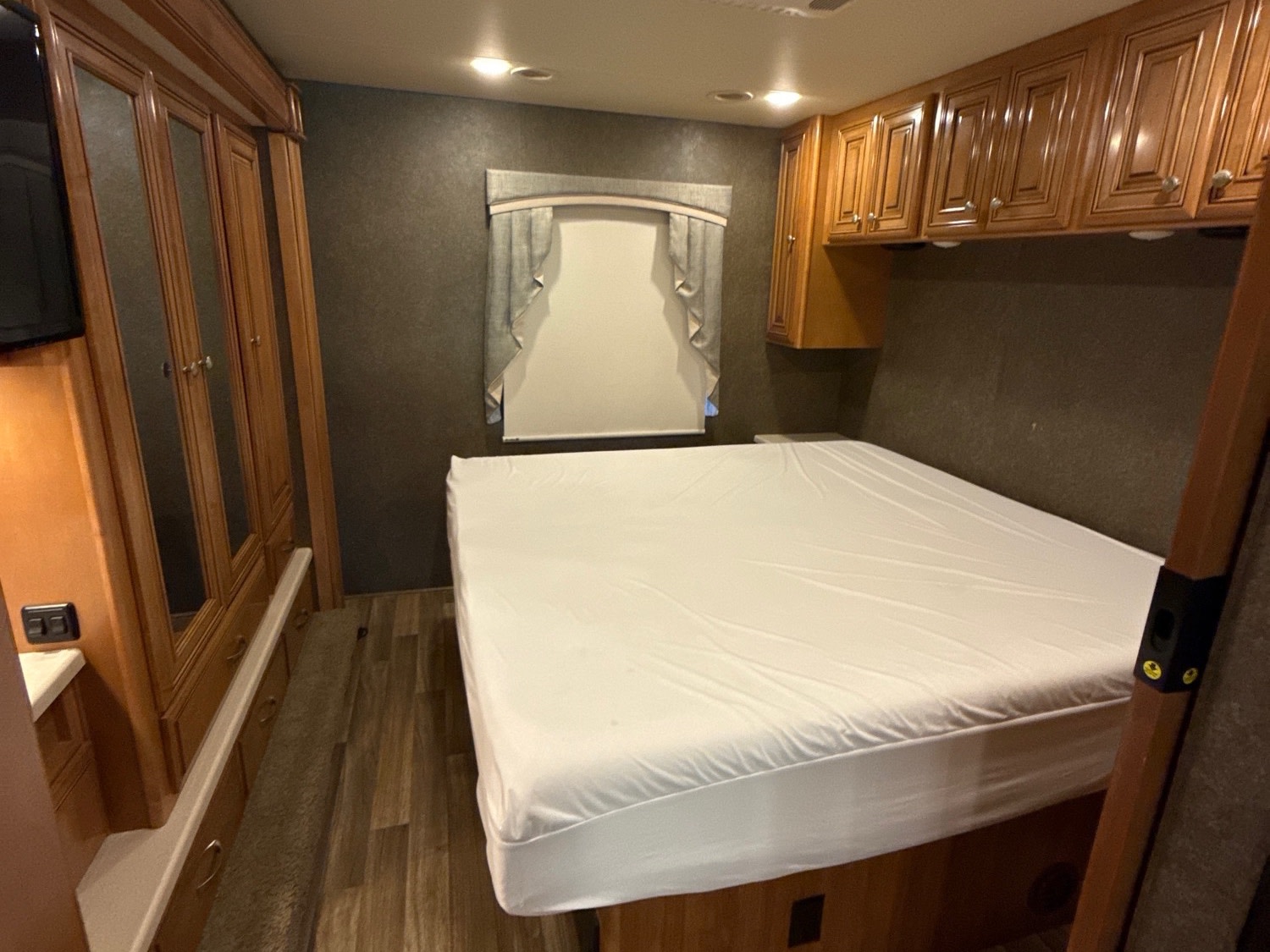 Inside an RV rental: a cozy bedroom features a queen bed, wood cabinets, a mirrored wardrobe, and window.. Thor Miramar 2017