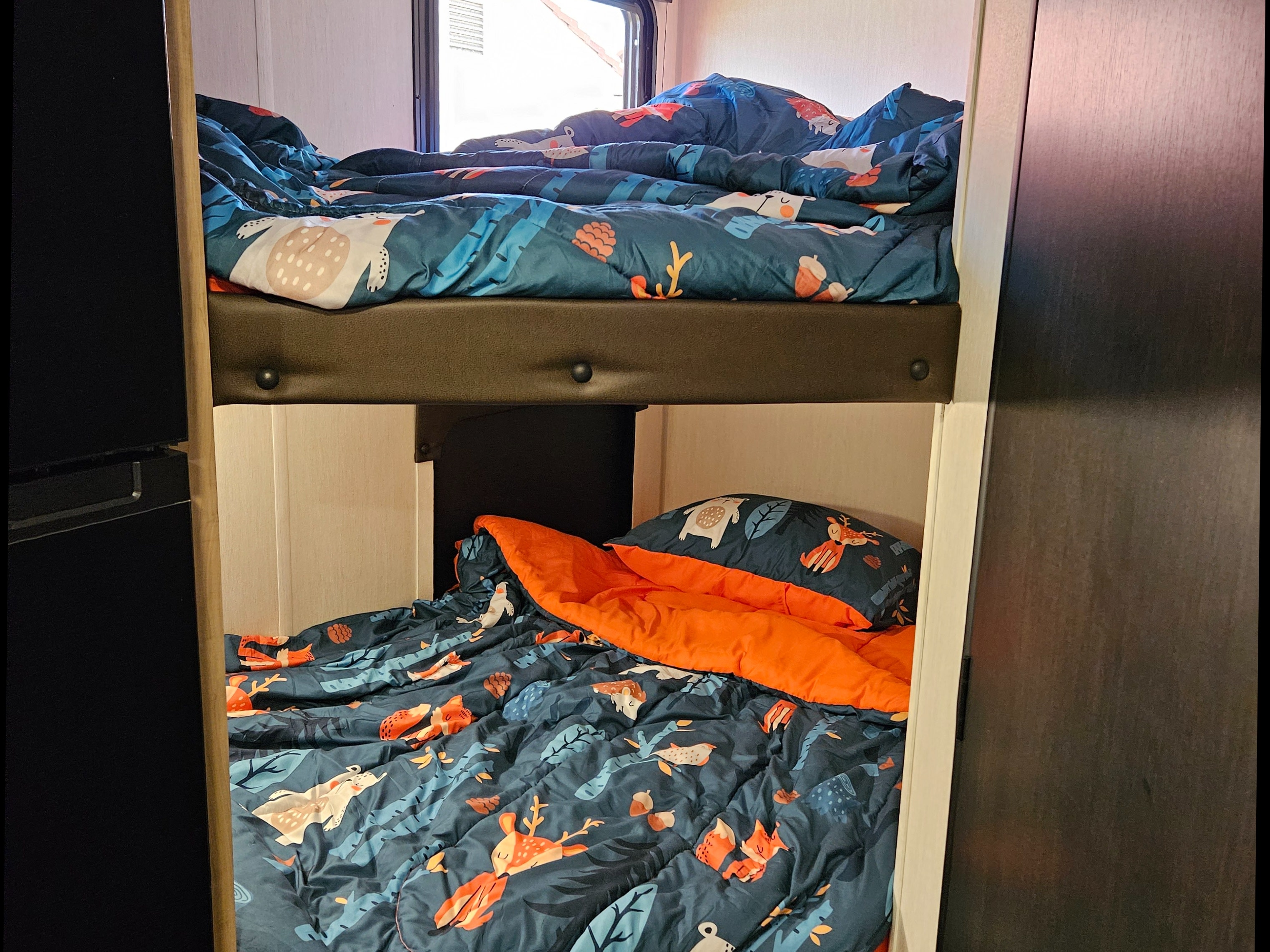 RV rental bunk beds with colorful animal and nature-themed comforters, bright orange sheet, and window view.. Forest River Cherokee Wolf Pup 2026