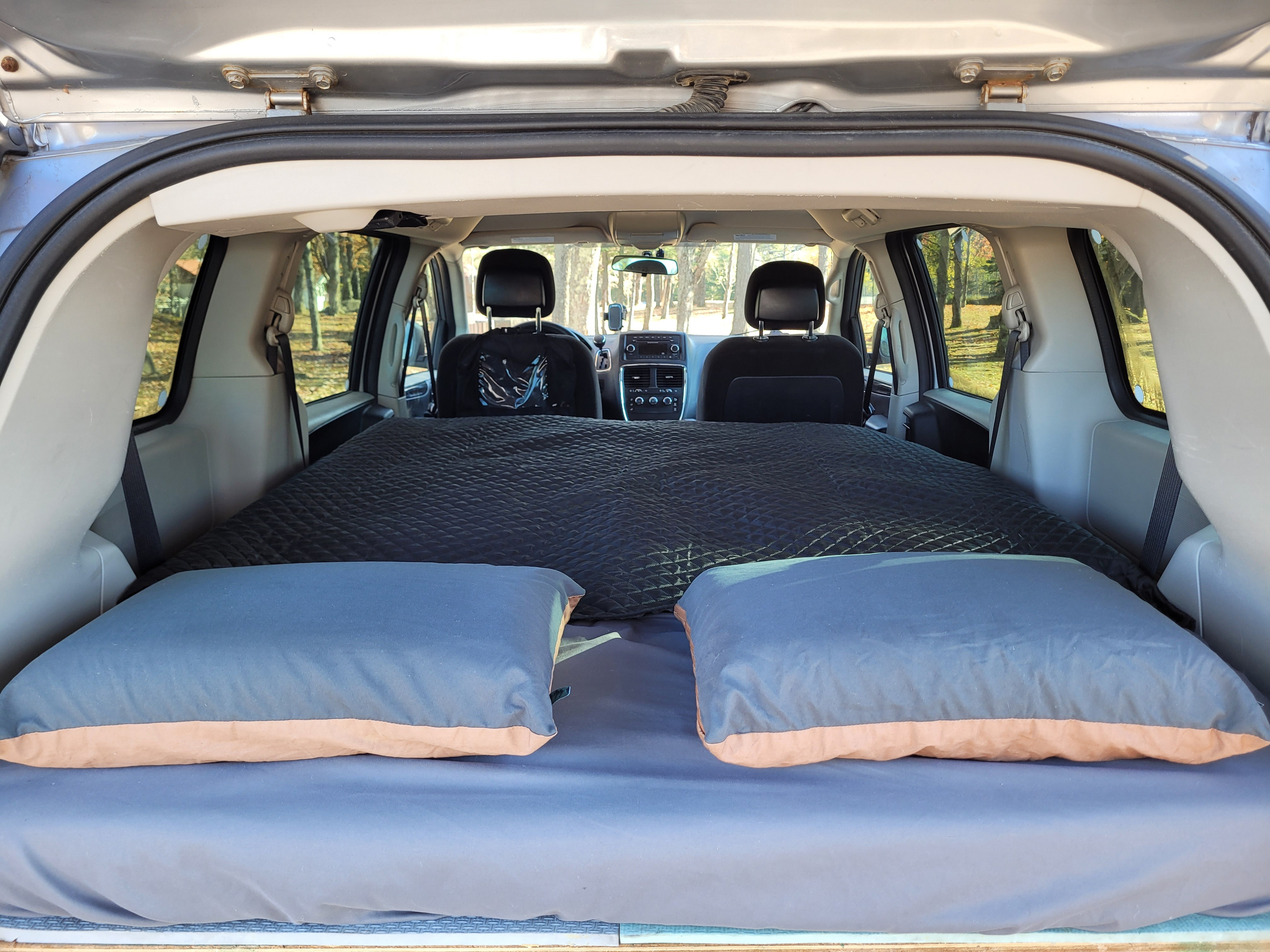 RV rental ready: A comfy minivan bed setup complete with pillows and blankets, perfect for car camping adventures.. Dodge Grand Caravan 2014