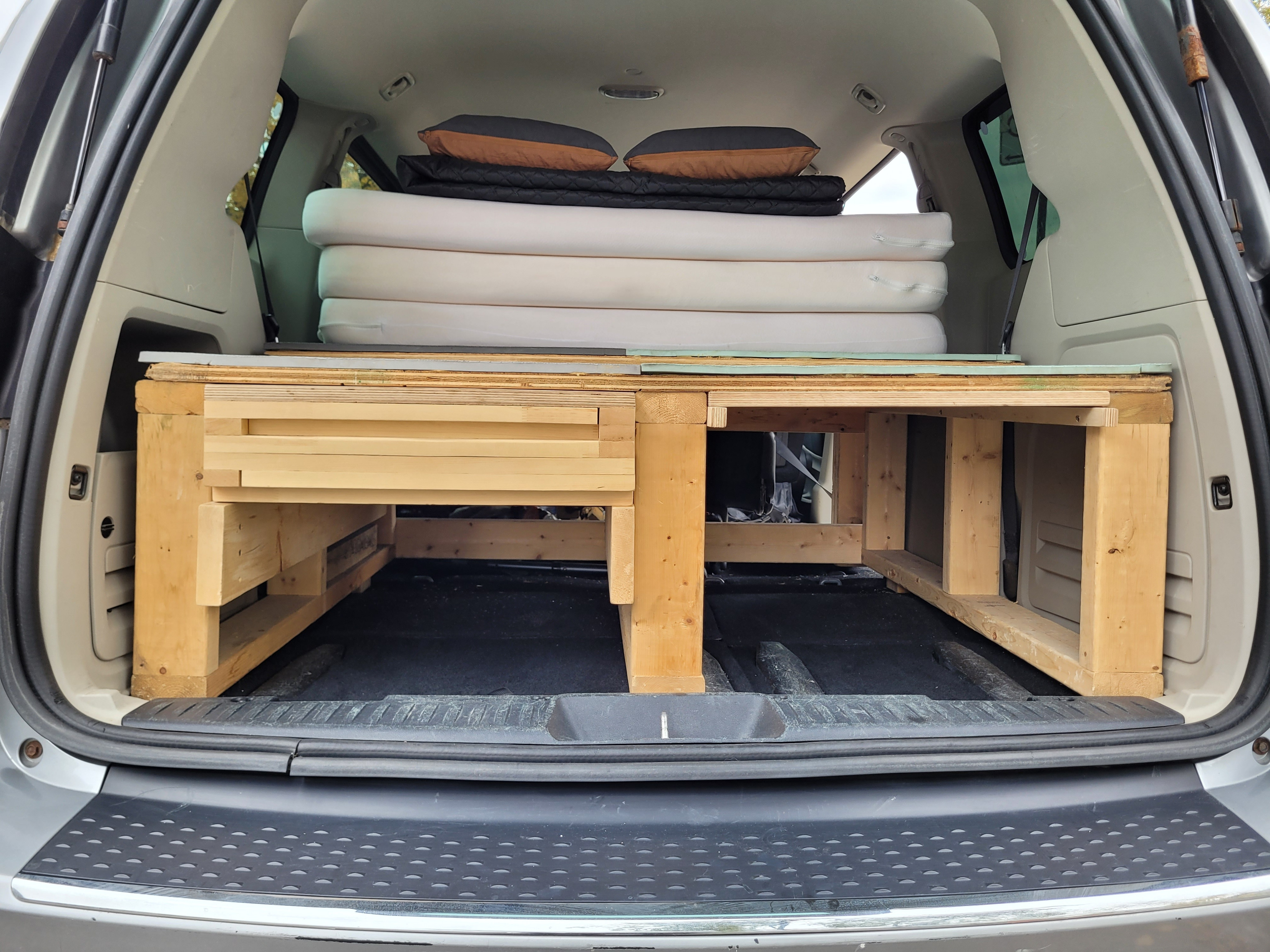 Minivan back with a custom wooden bed platform, stacked mattresses & pillows. Great for a DIY camper or rv rental adventure.. Dodge Grand Caravan 2014