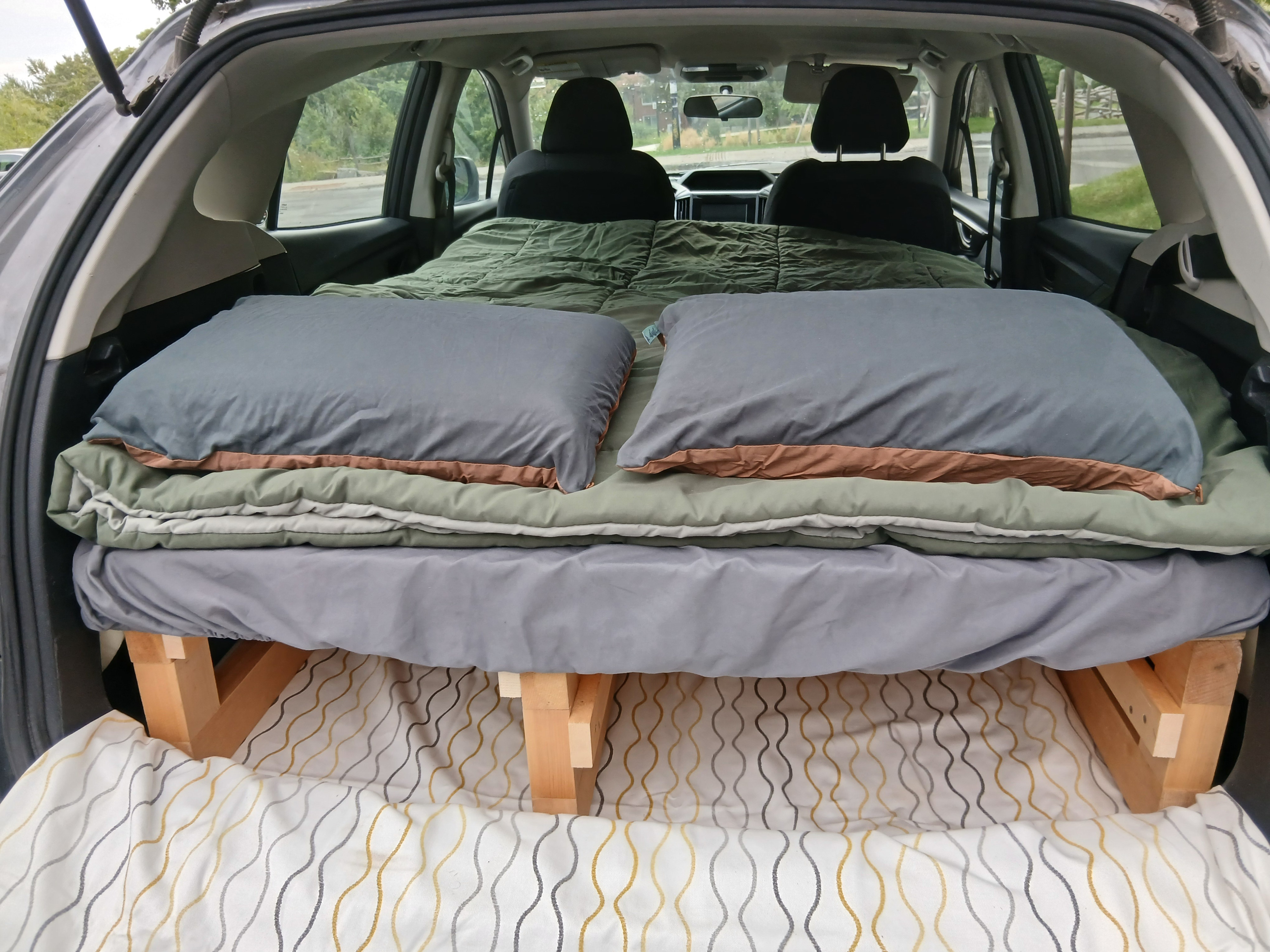 Inside an SUV, a custom wooden sleeping platform with soft bedding creates a cozy bed for car camping, perfect for your next rv rental adventure.. Subaru Impreza 2018