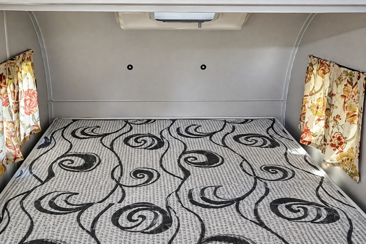 Cozy RV rental sleeping area with a bed, black & white patterned mattress, floral curtains, and overhead vent.. Coachmen Clipper 2022