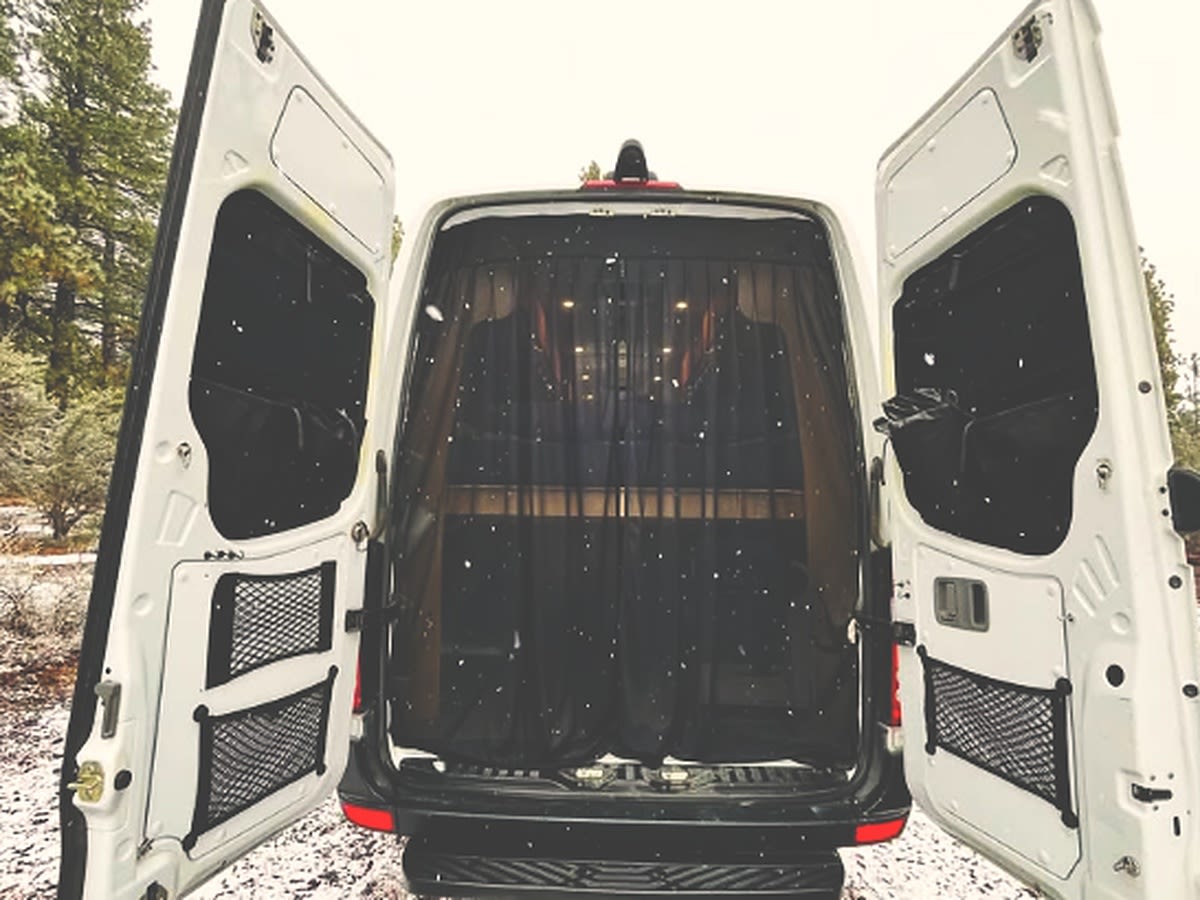 Adventure-ready rv rental camper van in a snowy forest. Open rear doors reveal a cozy, screened interior for winter travel.. Van Cruiser United Haven Custom Built 2015