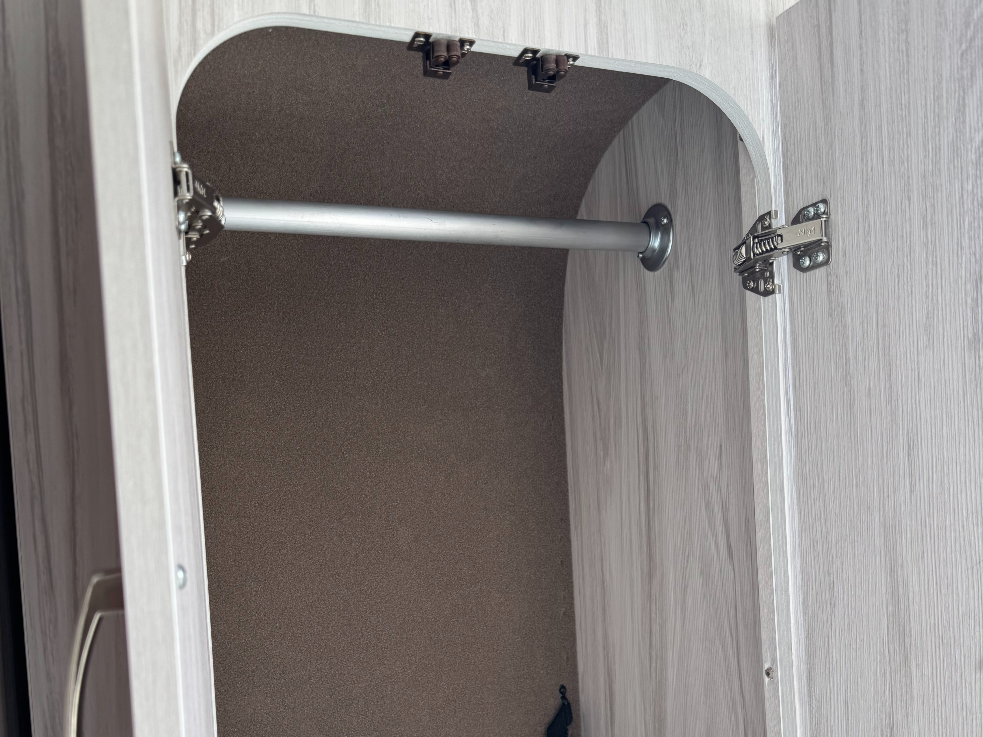 Open closet with hanging bar in an RV rental, featuring light wood grain trim and a dark, textured interior for storage.. Entegra Coach ARC 2025