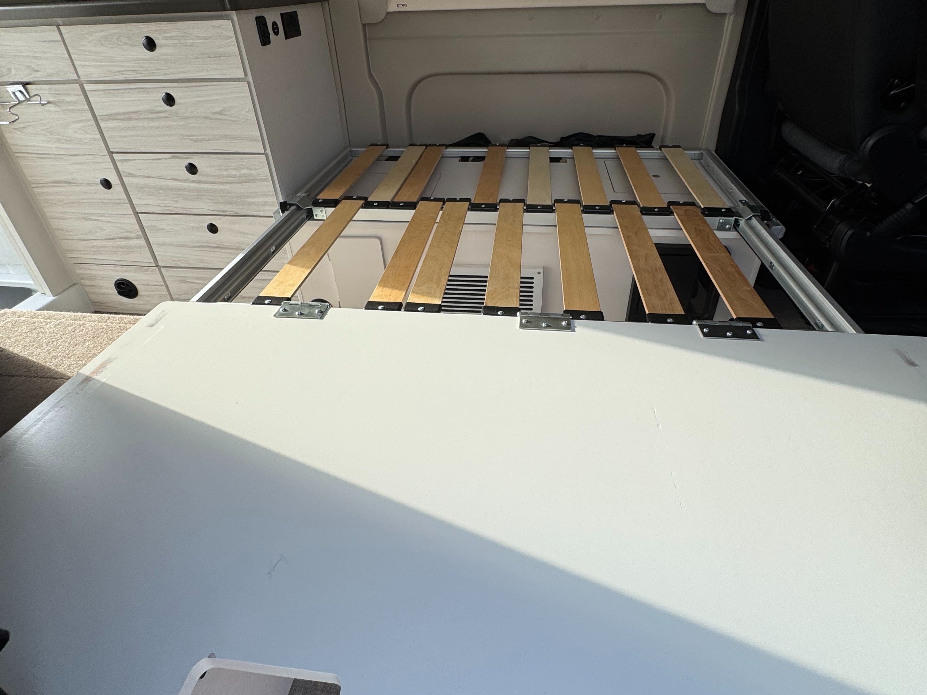 RV rental interior featuring a modular bed frame with wooden slats, storage cabinets, and a folding bed extension.. Entegra Coach ARC 2025