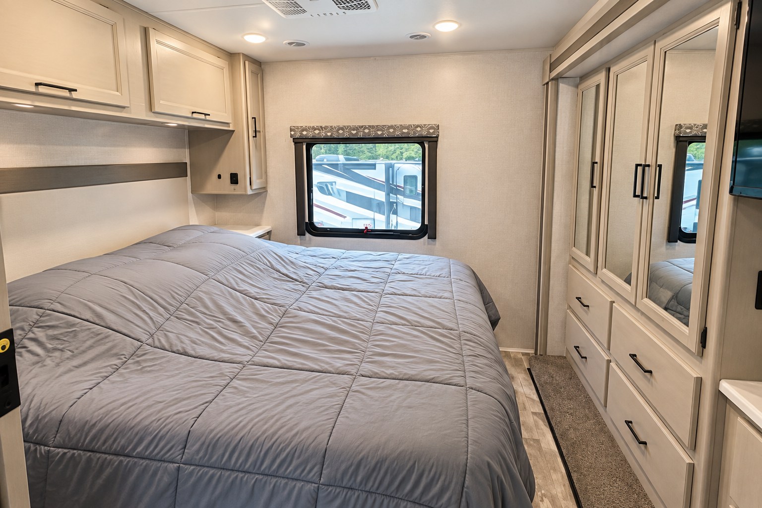 Explore this modern RV rental bedroom, featuring a comfortable bed with grey comforter, overhead storage, and a mirrored wardrobe.. Thor Windsport 2023