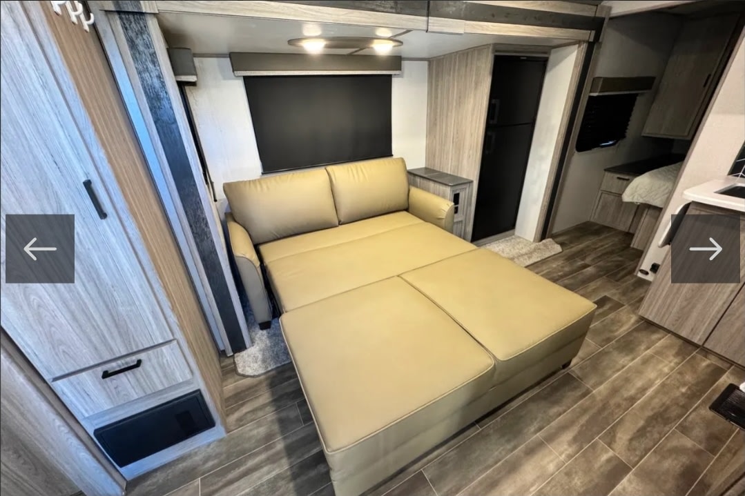 This RV rental features a versatile tan sofa bed, fully extended for sleeping, maximizing the compact living space.. Keystone RV Passport GT 2022