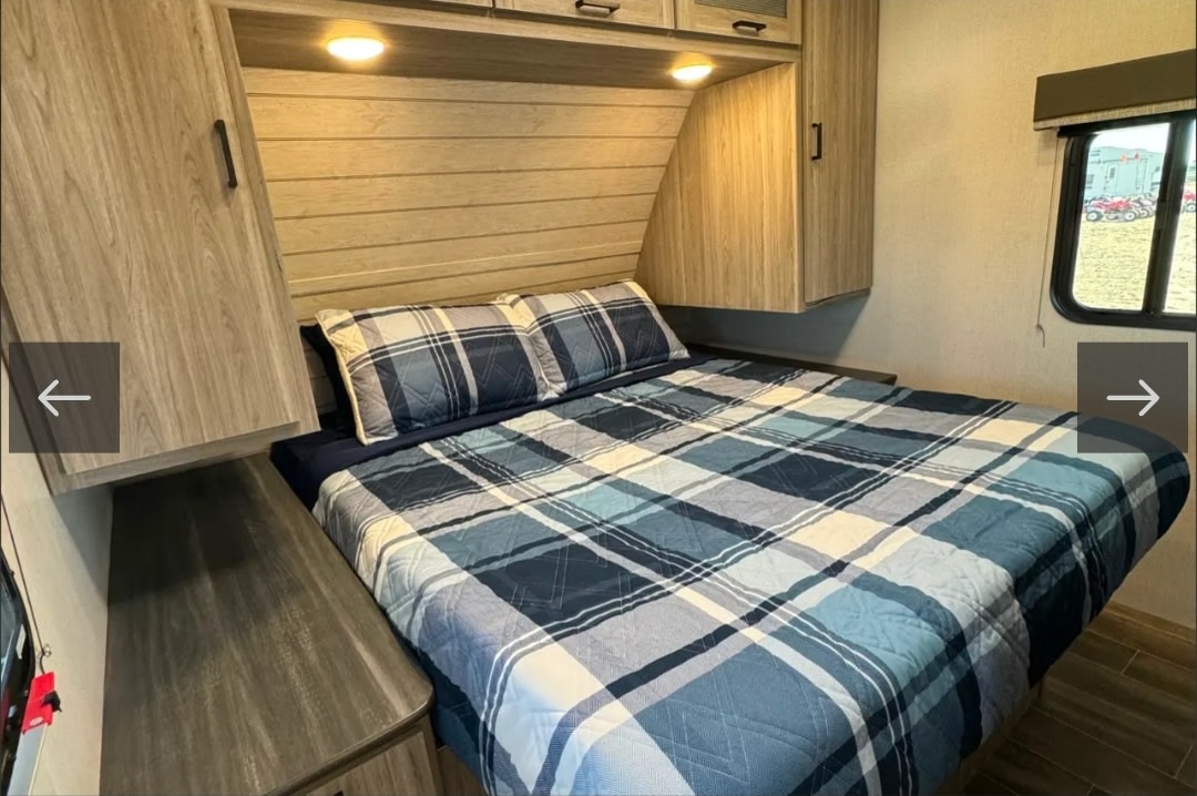 Cozy RV rental bedroom with a comfy plaid bed, wooden cabinets, and a scenic window view for your travels.. Keystone RV Passport GT 2022