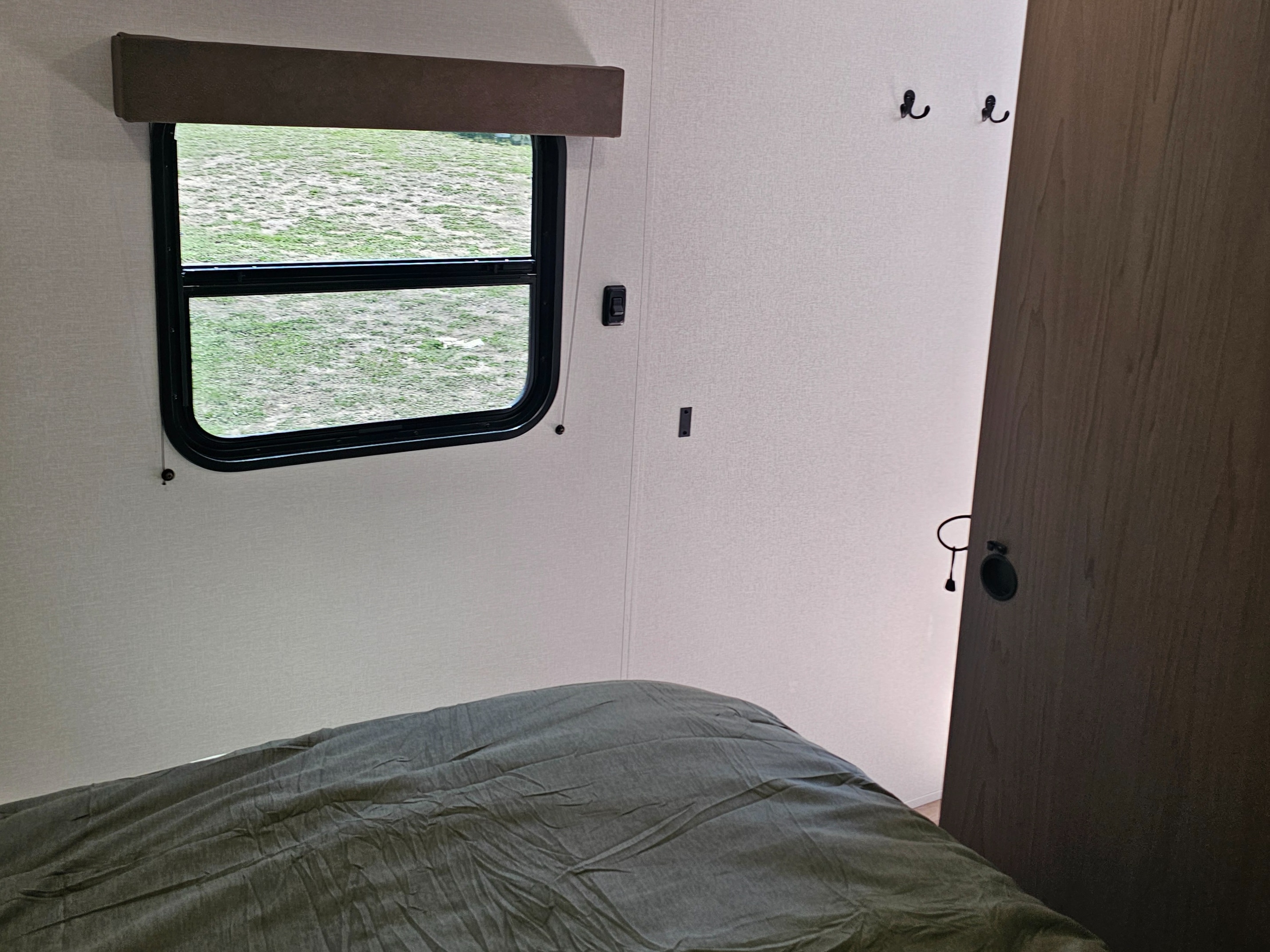 Cozy rv rental bedroom interior featuring a window with a green view, a comfortable bed, and wall hooks.. Grand Design Transcend Xplor 2026
