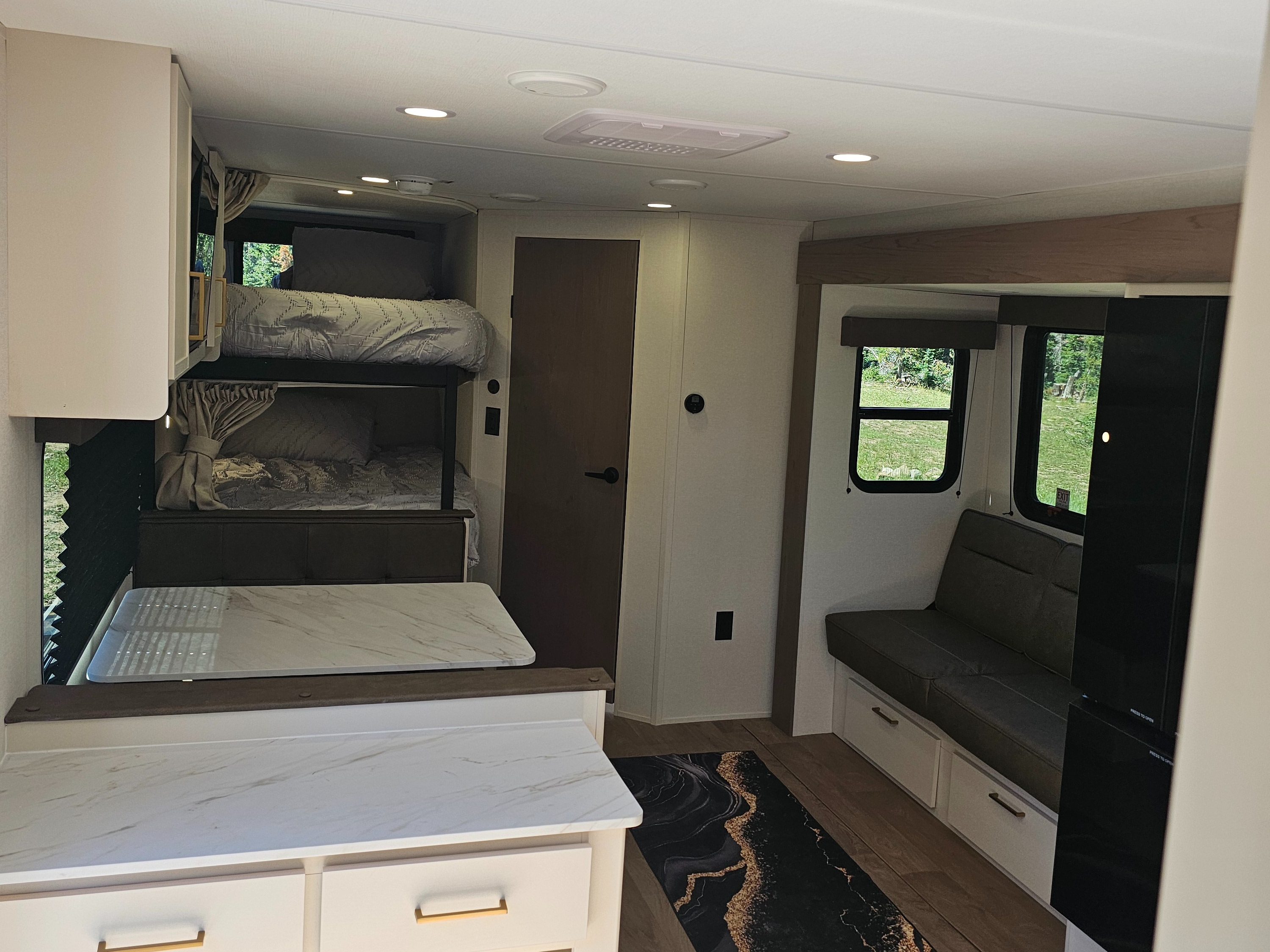 Modern rv rental interior: bunk beds, sleek kitchenette, and a cozy sofa by windows offering outdoor views, ready for your adventure.. Grand Design Transcend Xplor 2026