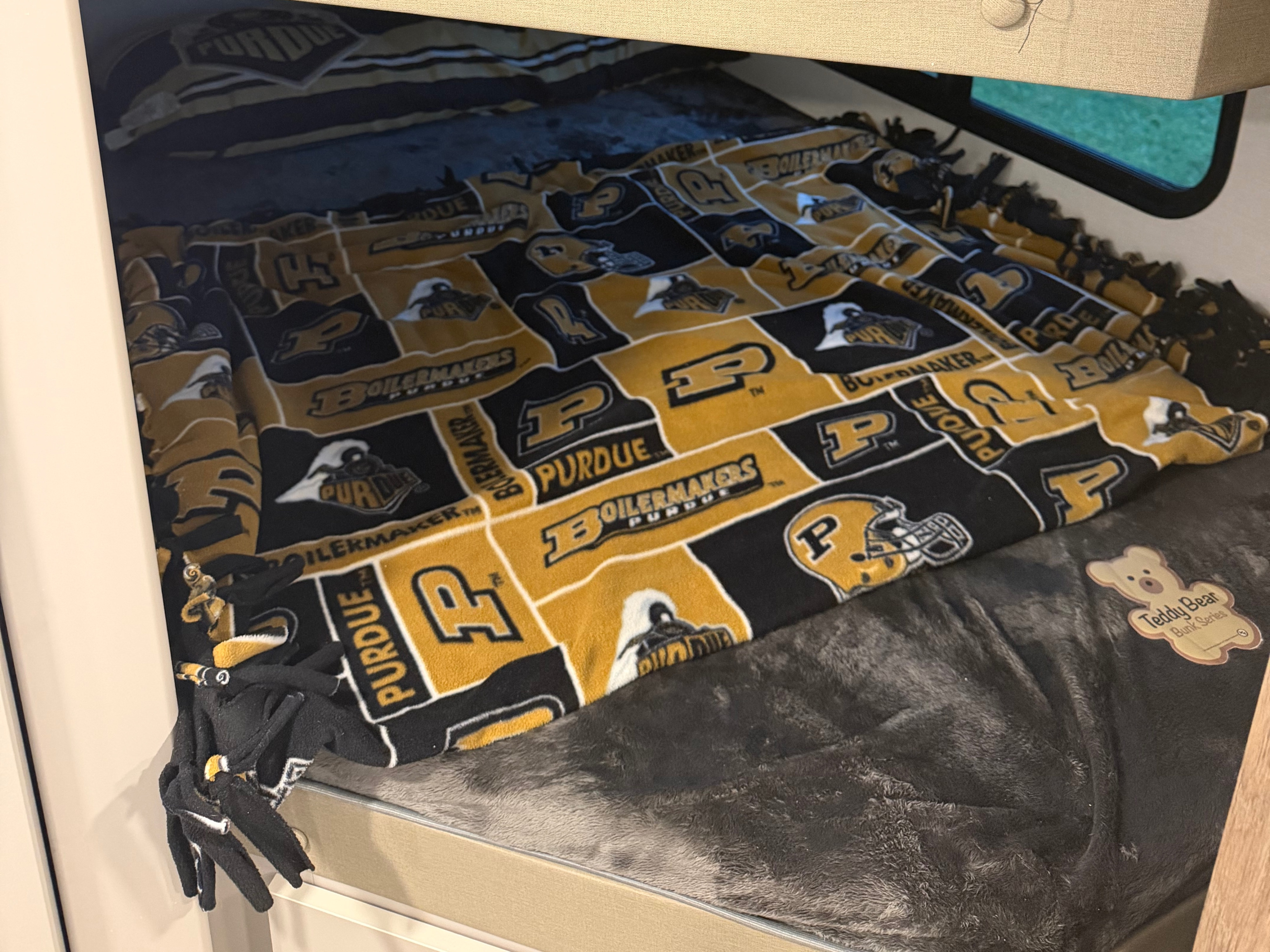 Cozy Purdue bunk bed with a gold and black blanket in an RV rental. Perfect for fans on the go!. Alliance RV Delta Ultra Light 2026