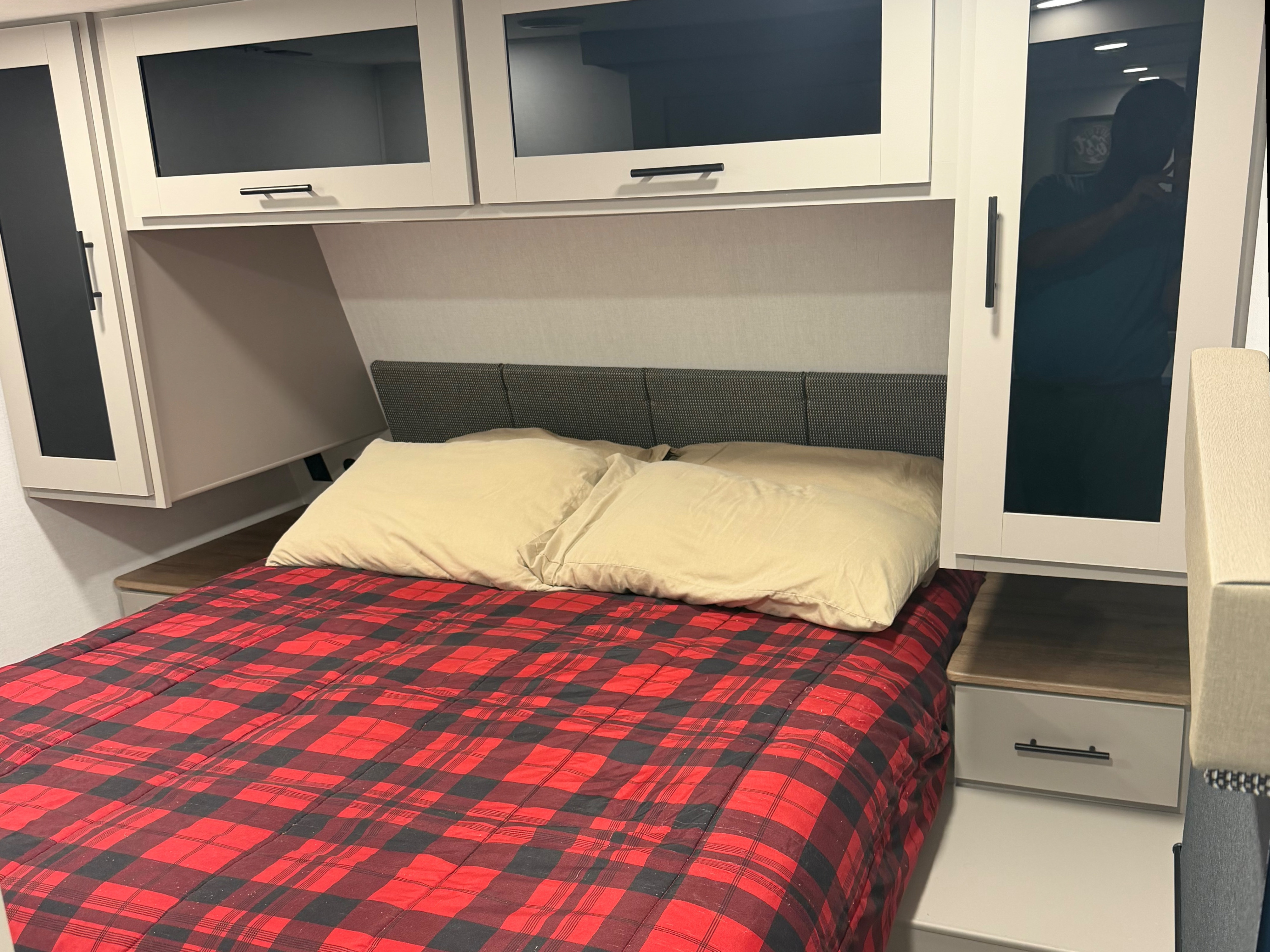 Comfortable RV rental bedroom featuring a red plaid bed, light pillows, and ample overhead cabinet storage.. Alliance RV Delta Ultra Light 2026