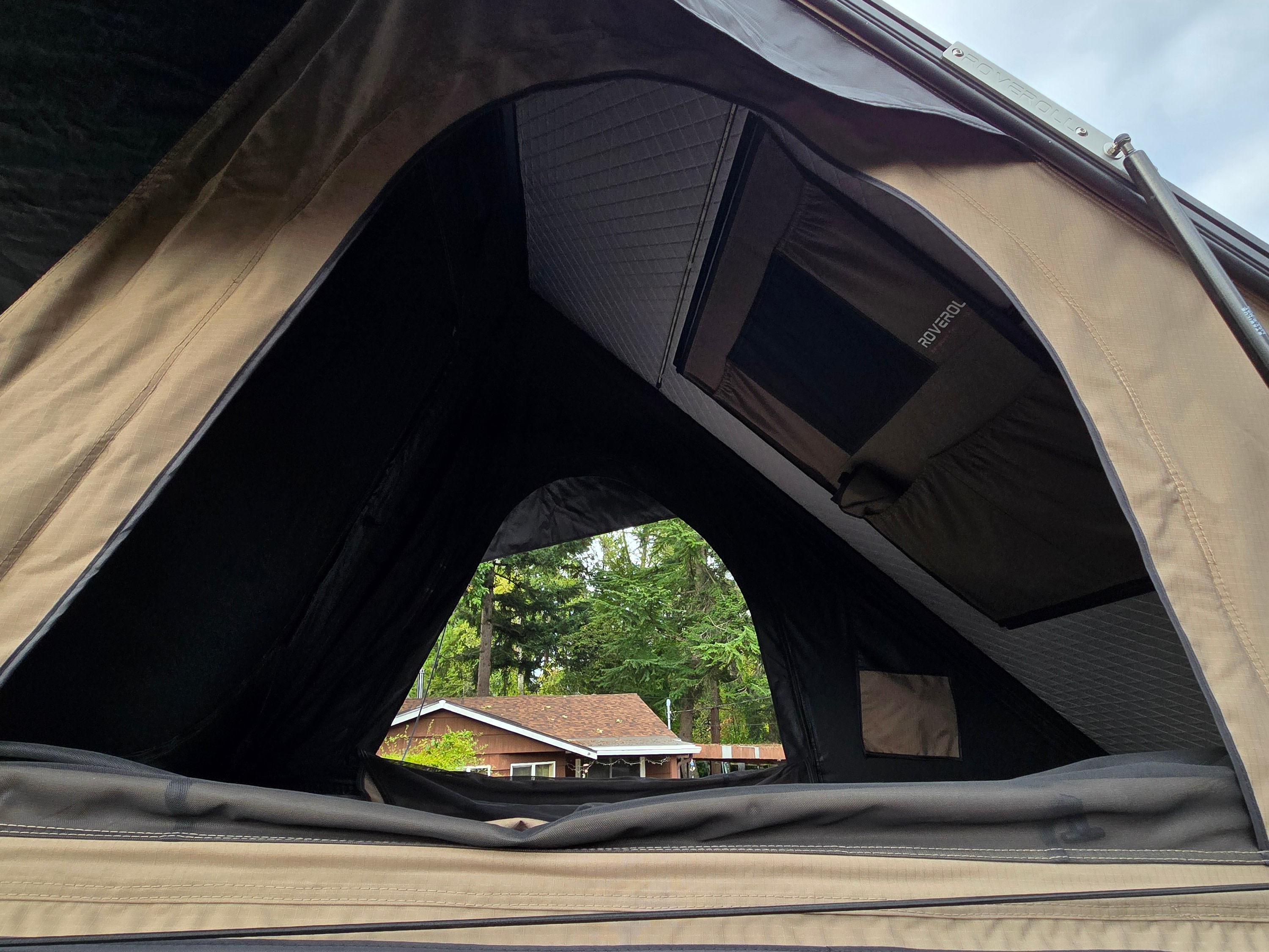 Interior view of a Roverol rooftop tent, a cozy part of your RV rental. Looking out at a house & trees through the mesh opening.. Ford Transit 2017