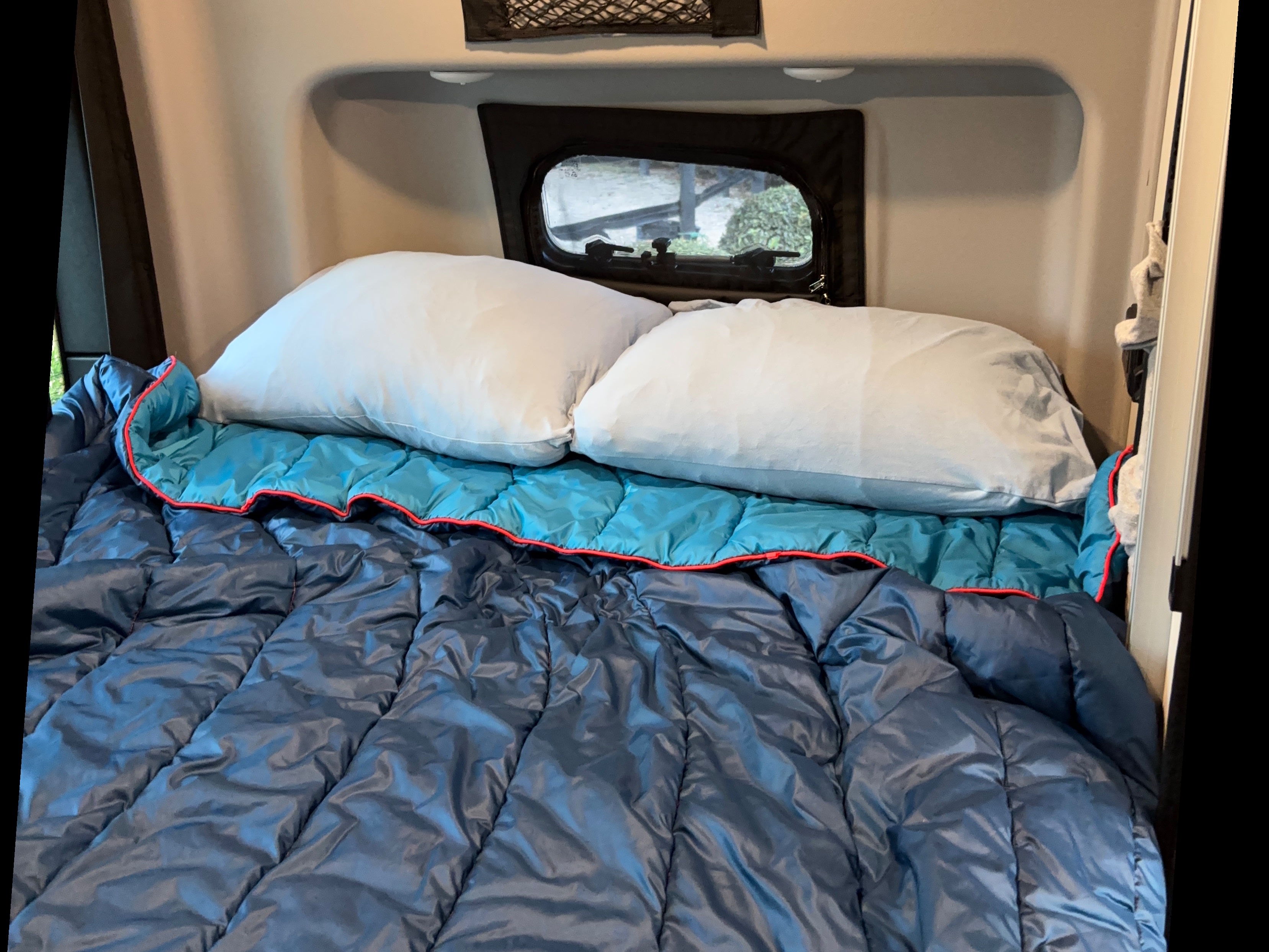 Cozy rv rental sleeping area featuring two pillows, a light blue blanket with red trim, and a darker blue comforter.. Winnebago Revel 2025
