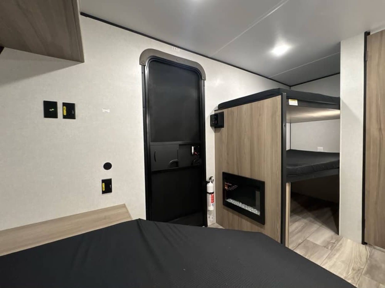 RV rental interior: view of bunk beds, an electric fireplace, a main bed, and an entry door. Modern and functional space.. Keystone by Coleman 13B 2027