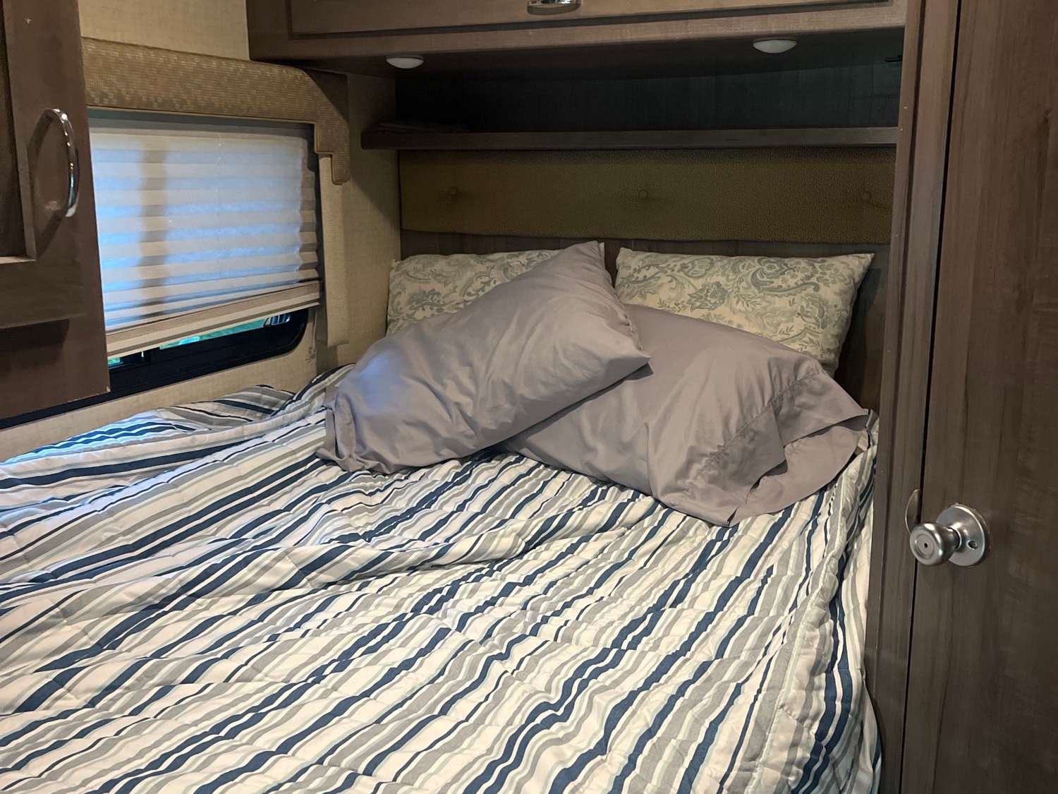 RV rental bedroom showcasing a striped bed, two pillows, and window blinds. A compact and comfortable sleeping space for travel.. Winnebago Minnie Winnie 2018