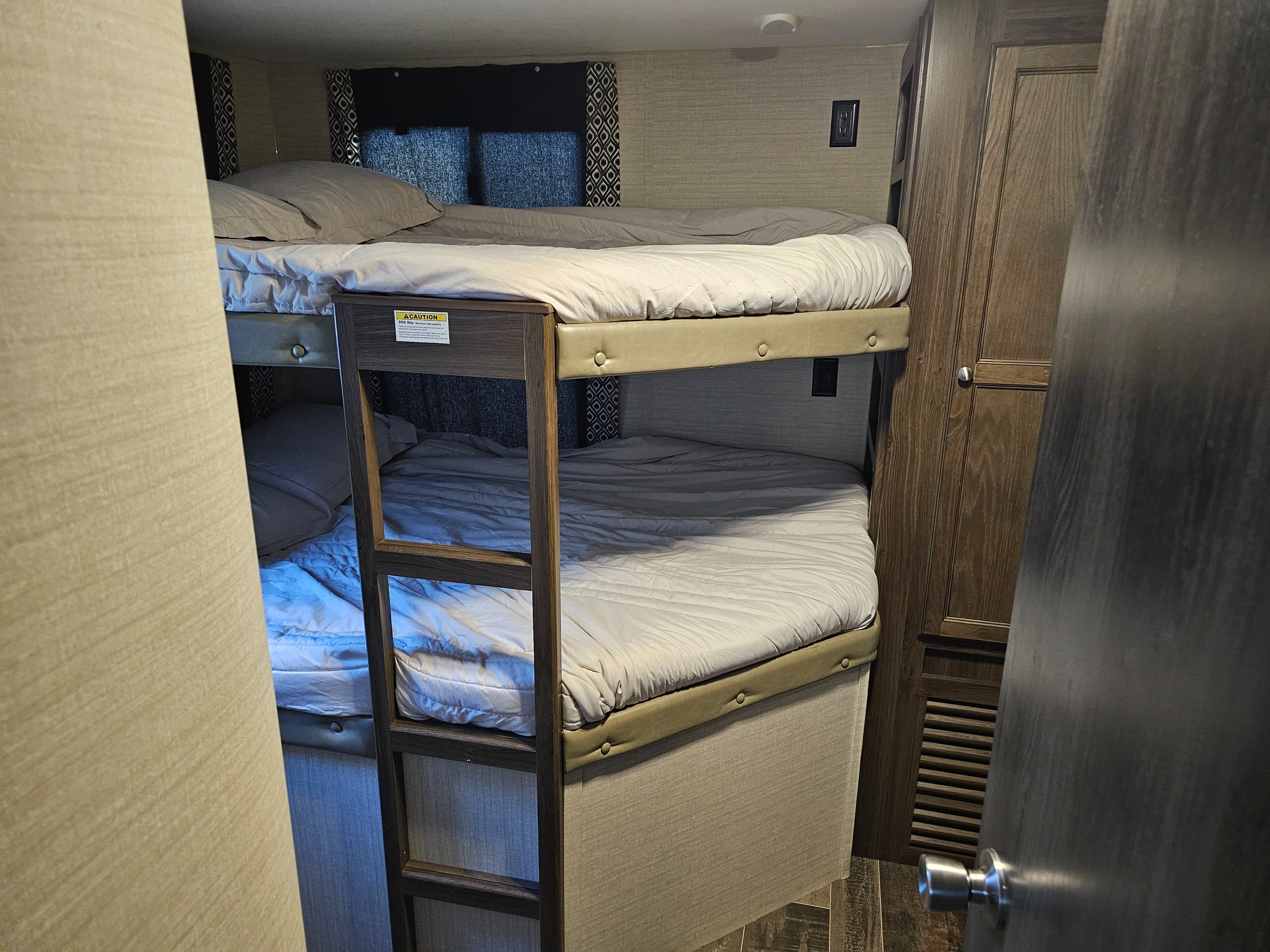 Cozy RV rental bunk beds: a sleeping area with two beds, a ladder, and a wooden closet inside a camper.. Keystone RV Bullet Ultra Lite 2018