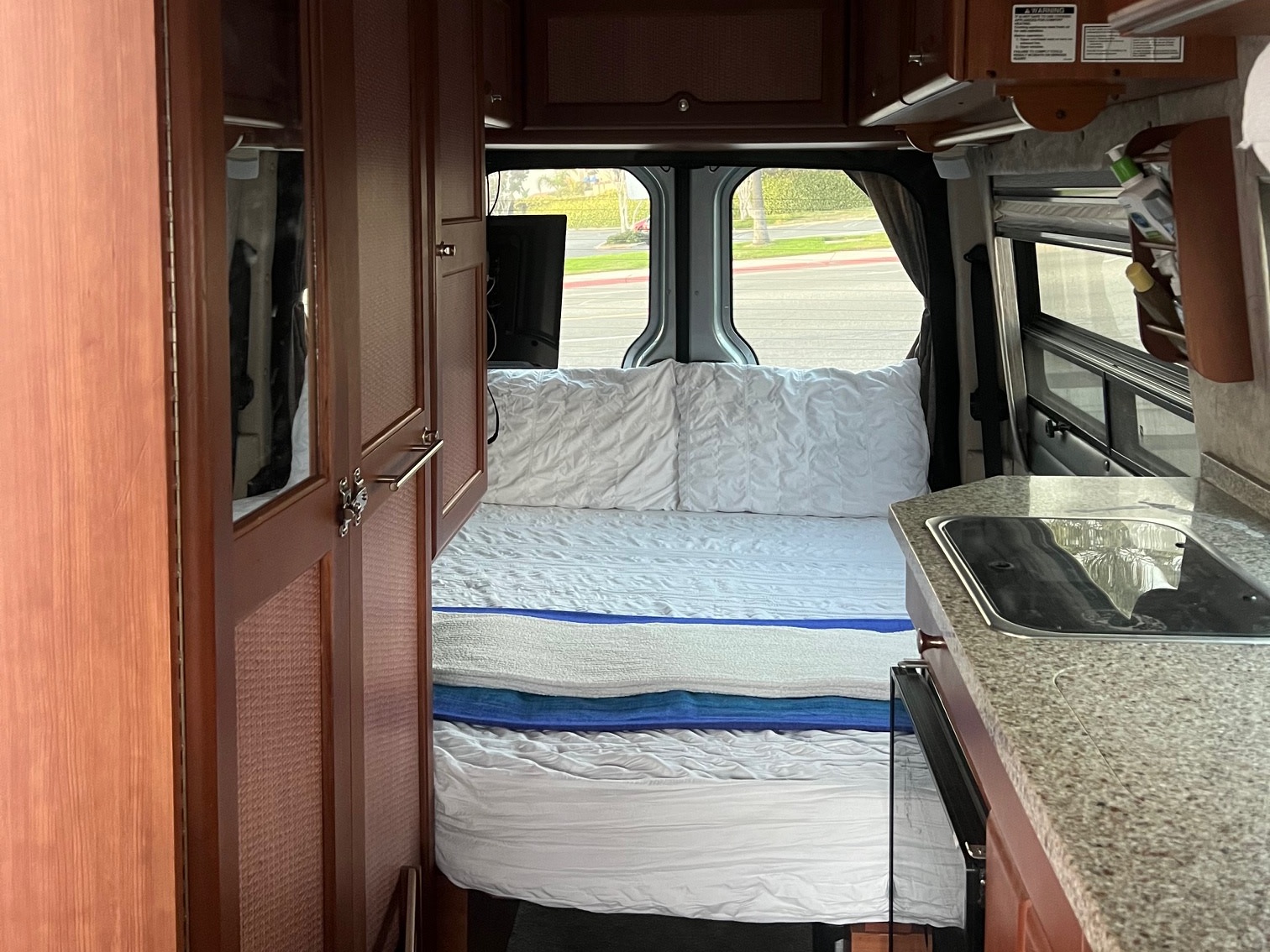 RV rental interior: a comfy bed with white linens, wood cabinetry, and a granite-top kitchen with a sink.. Roadtrek Roadtrek Class B 2007