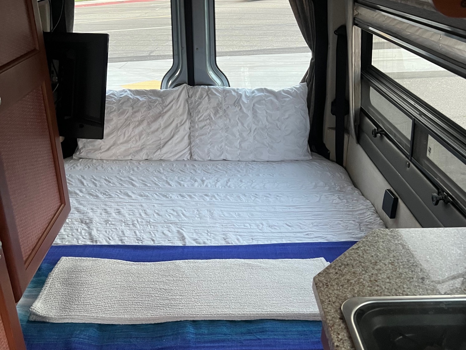 Inside a cozy rv rental: bed with white bedding, wall-mounted TV, and a compact kitchen counter with sink.. Roadtrek Roadtrek Class B 2007
