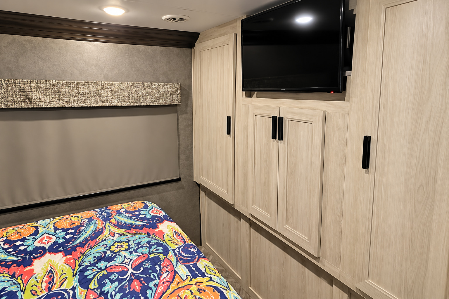 RV rental bedroom with light wood cabinets, TV, and vibrant paisley bedding. A roller blind covers the window.. Forester Classic 2021
