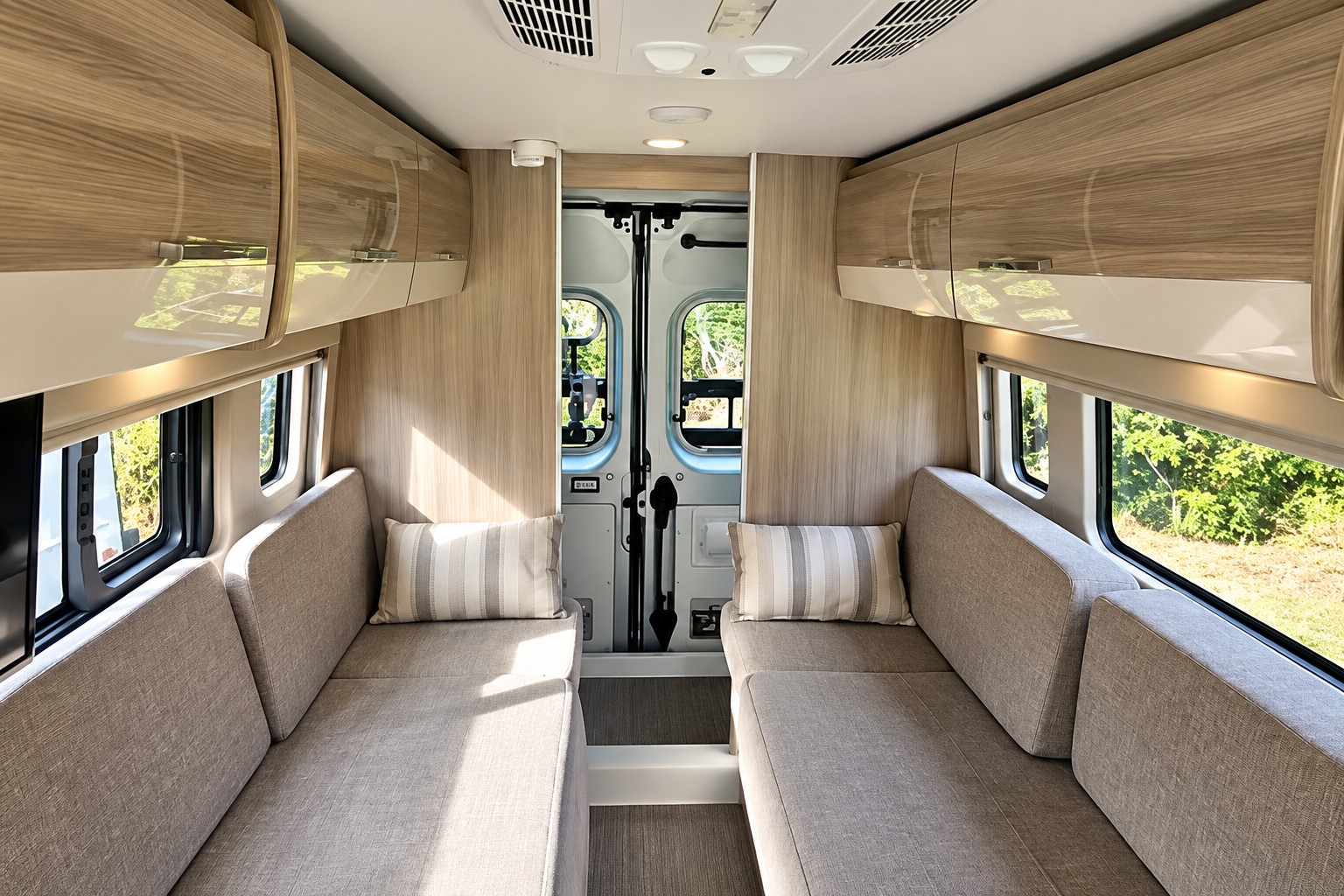 Spacious and modern interior of an RV rental, featuring comfortable benches, overhead storage, and large windows for scenic views.. Thor sequence 2023