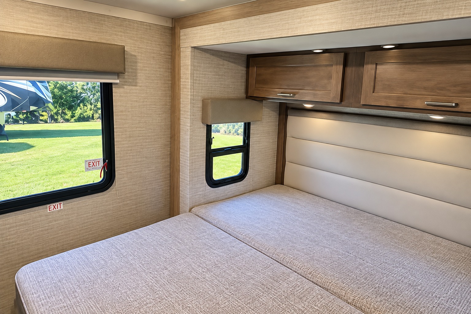 A bright rv rental bedroom featuring a split bed, windows overlooking a green field, and convenient overhead cabinets.. Winnebago Minnie Winnie 2024