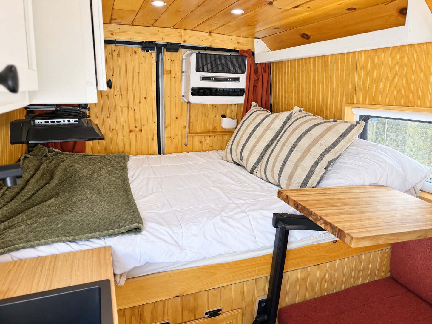 Inviting rv rental interior: warm wooden walls, a comfy bed with pillows, mounted TV, AC, and a handy swivel table.. Dodge Ram 2500 2024