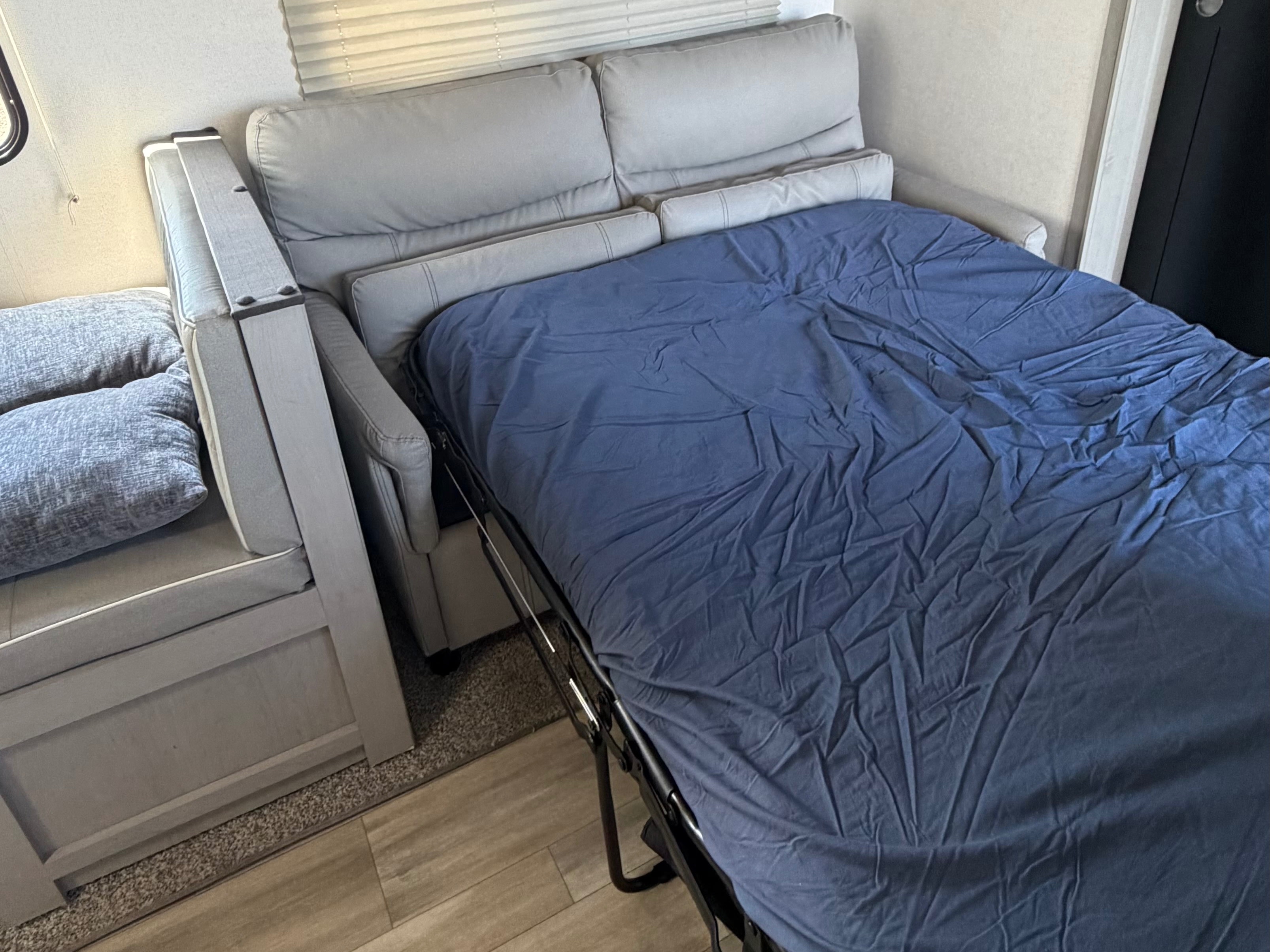 Cozy RV rental interior showing a gray sofa pulled out as a bed with a blue sheet, perfect for extra sleeping space.. Forest River Prime Time LE 2023