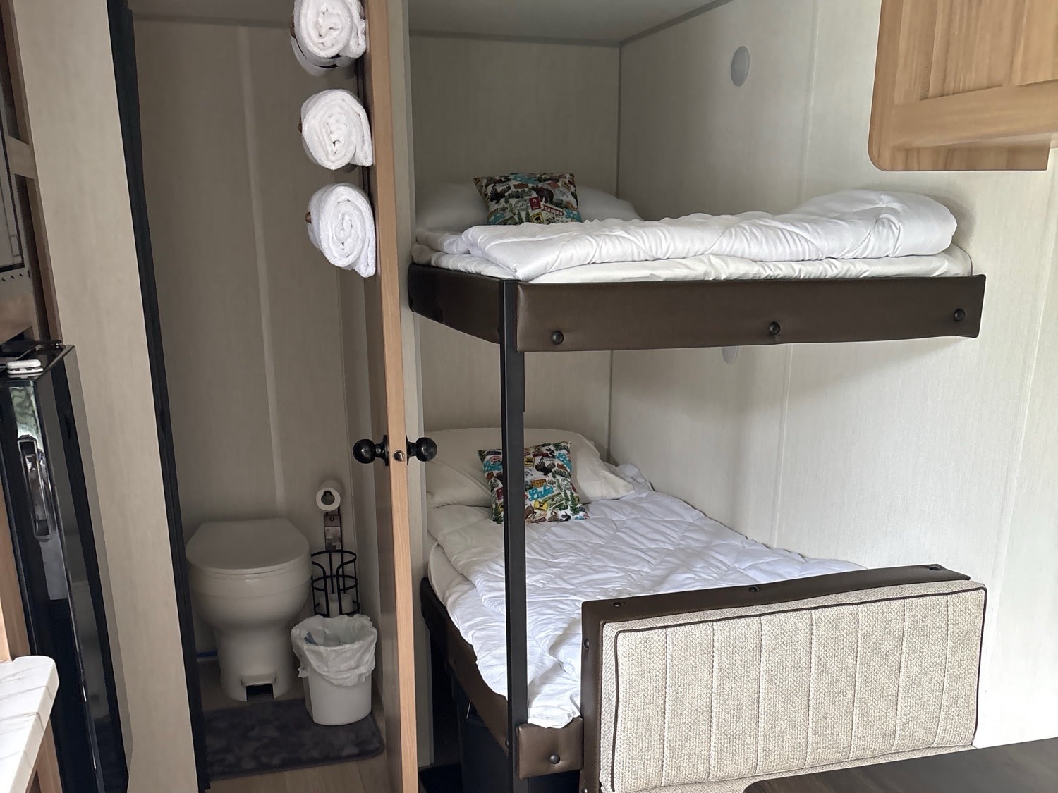 RV rental interior featuring bunk beds with white bedding, a compact toilet in a small bathroom, and rolled towels.. Forest River Cherokee Wolf Pup 2025