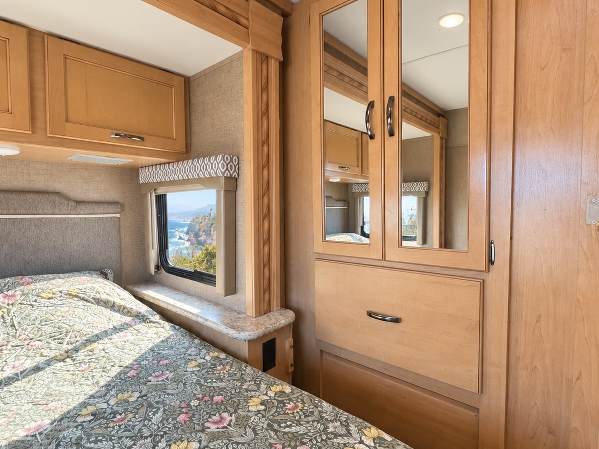 Cozy RV rental bedroom with a scenic ocean view. Features a comfortable bed, cabinets, and wardrobe for your next road trip.. Thor Freedom Elite 2018
