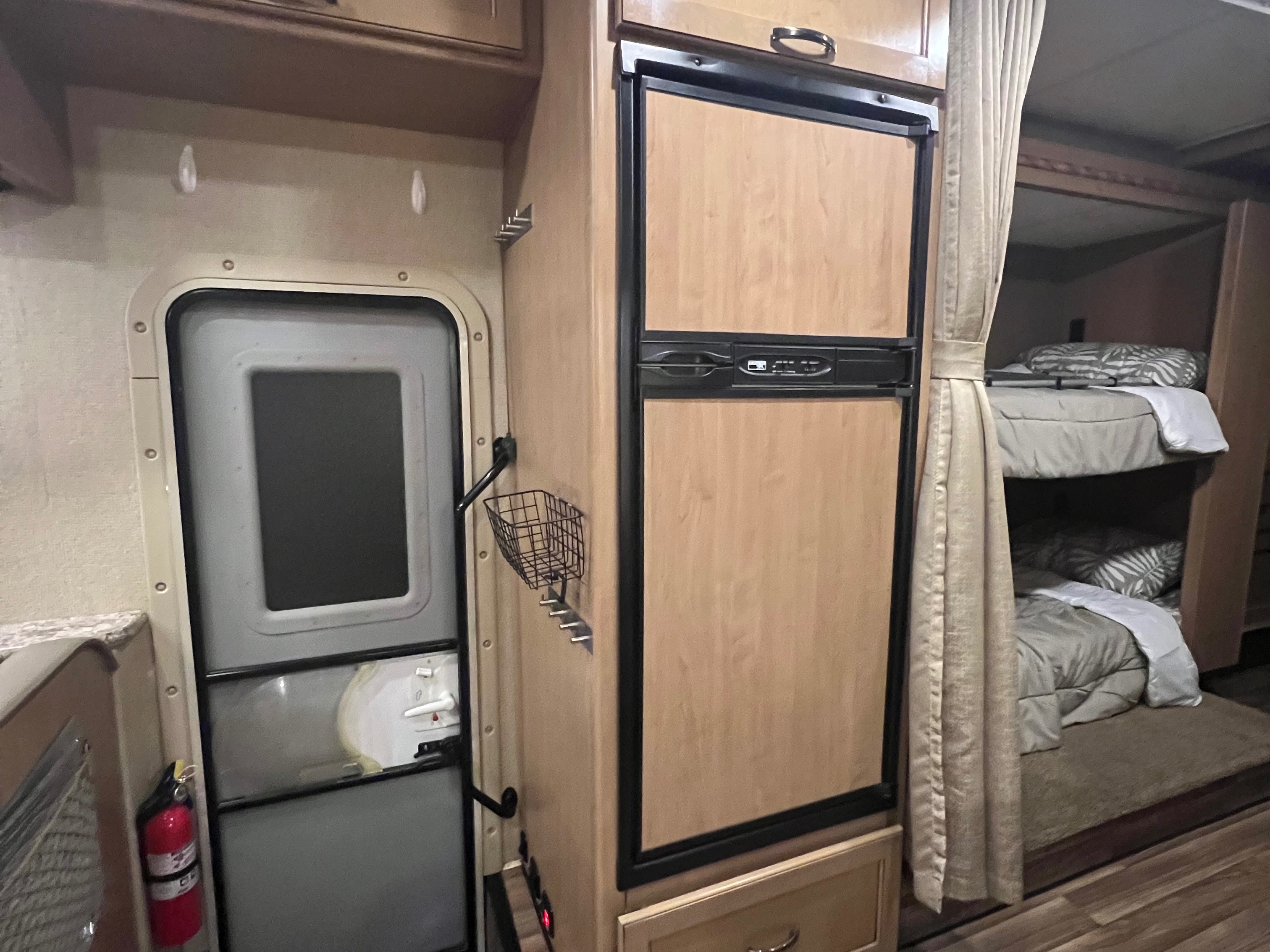 Inside this RV rental: built-in refrigerator, exit door with fire extinguisher, and bunk beds with privacy curtains.. Thor Four Winds 2018
