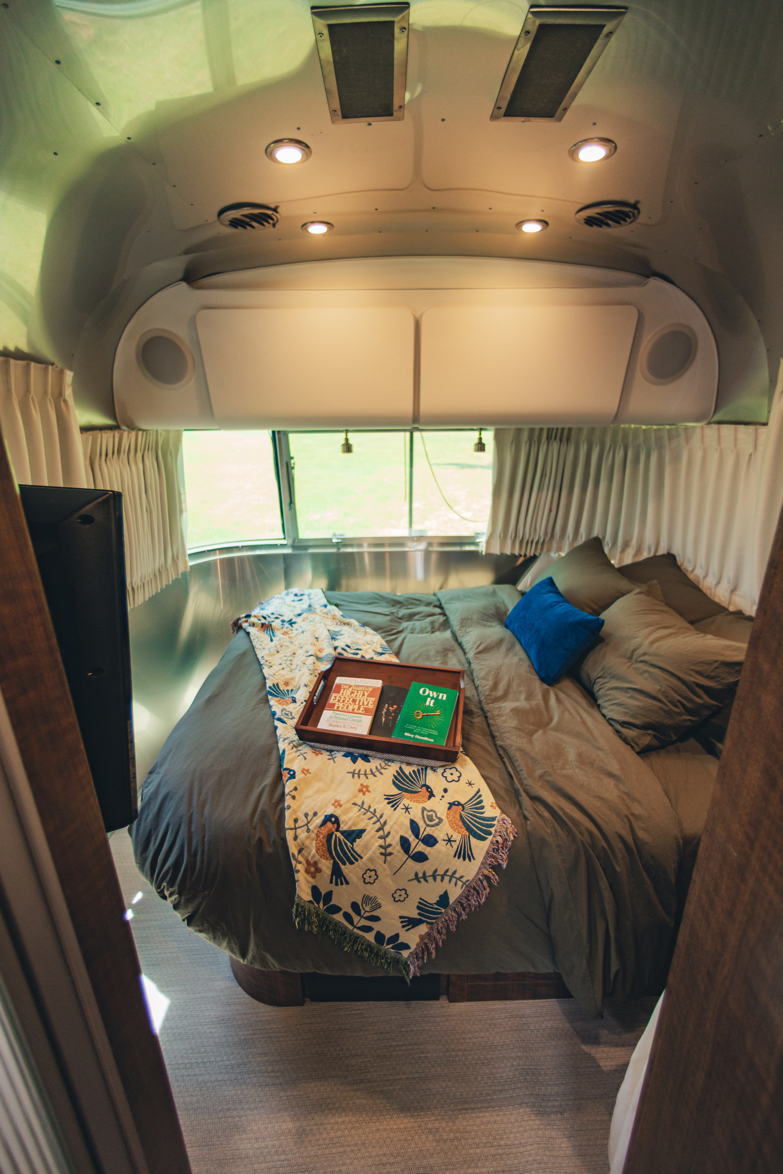 Cozy Airstream RV rental bedroom with a comfy bed, decorative blanket, and books for a relaxing getaway.. Airstream Globetrotter 2019