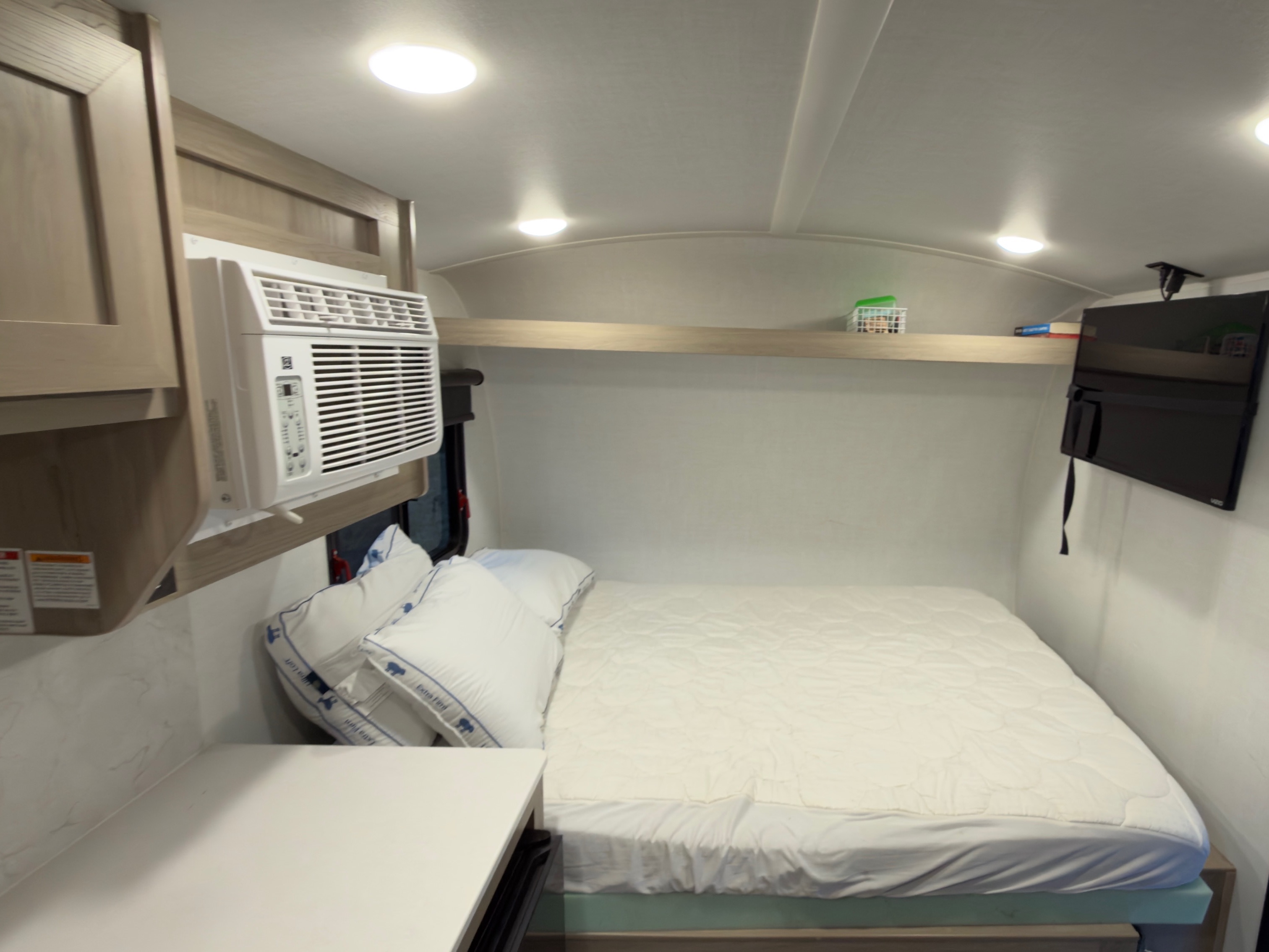 This rv rental bedroom shows a compact interior with a bed, wall-mounted AC, TV, and an overhead shelf for storage.. Forest River Rockwood Geopro 2026