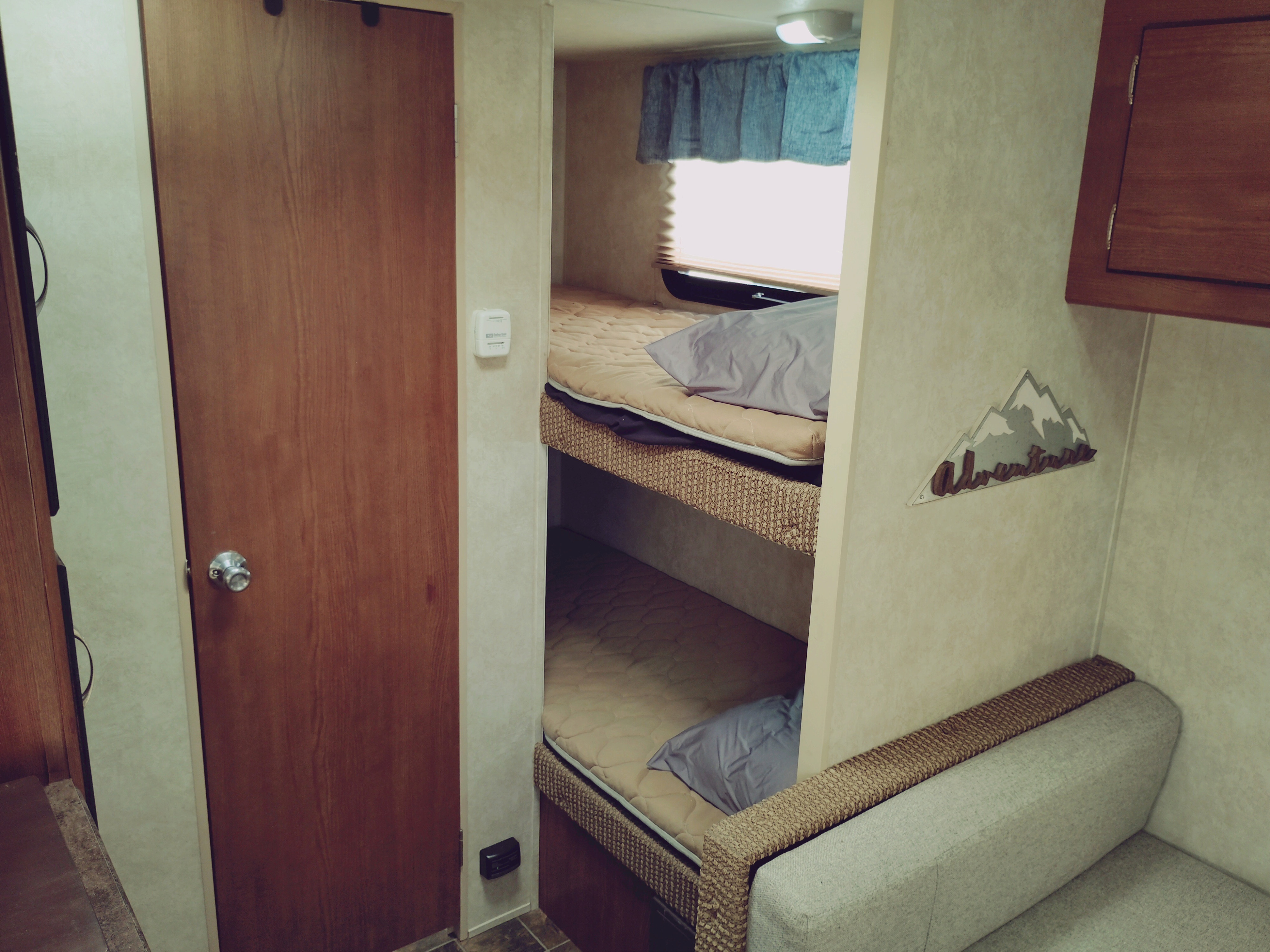 Cozy RV rental interior features bunk beds, a couch, a door, and an "Adventure" sign. Ideal for compact travel.. Forest River Salem Cruise Lite 2014