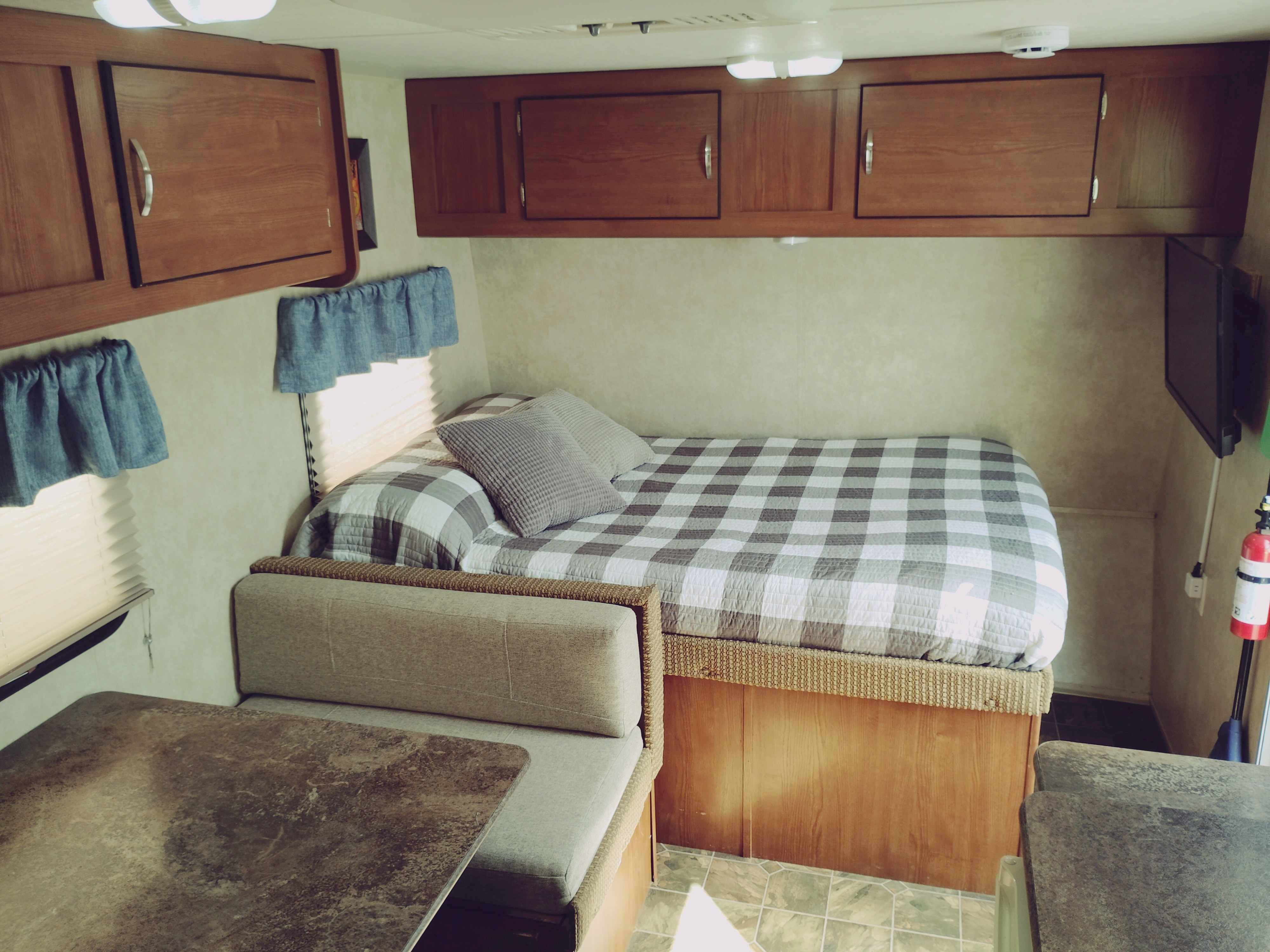 Inside an rv rental: A bed with gray plaid comforter, dinette seating, overhead cabinets, TV, and fire extinguisher.. Forest River Salem Cruise Lite 2014