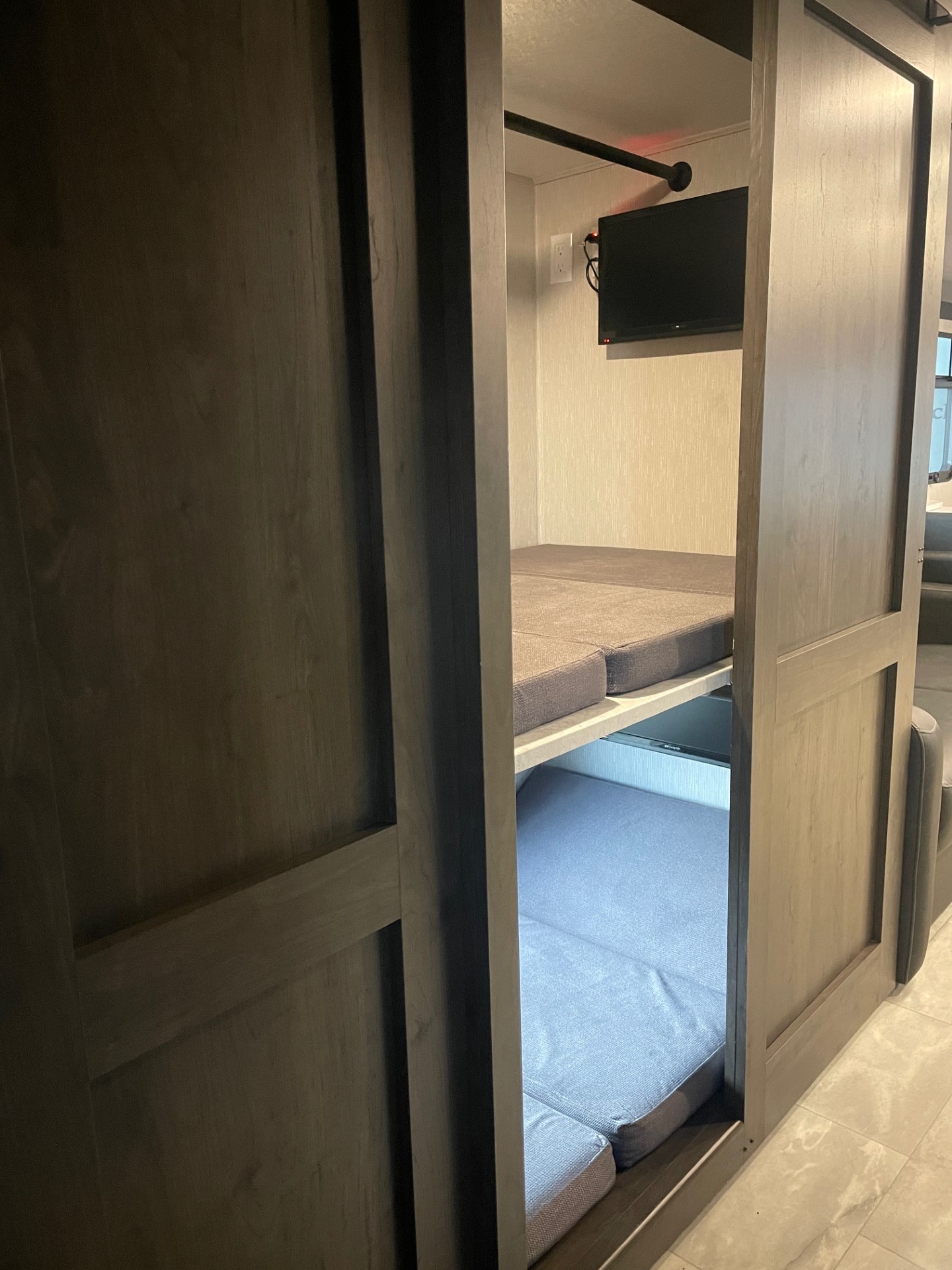 An RV rental interior with bunk beds. Two gray cushioned sleeping areas are visible, along with a wall-mounted TV.. Coachmen MIRADA 35ESF 2026