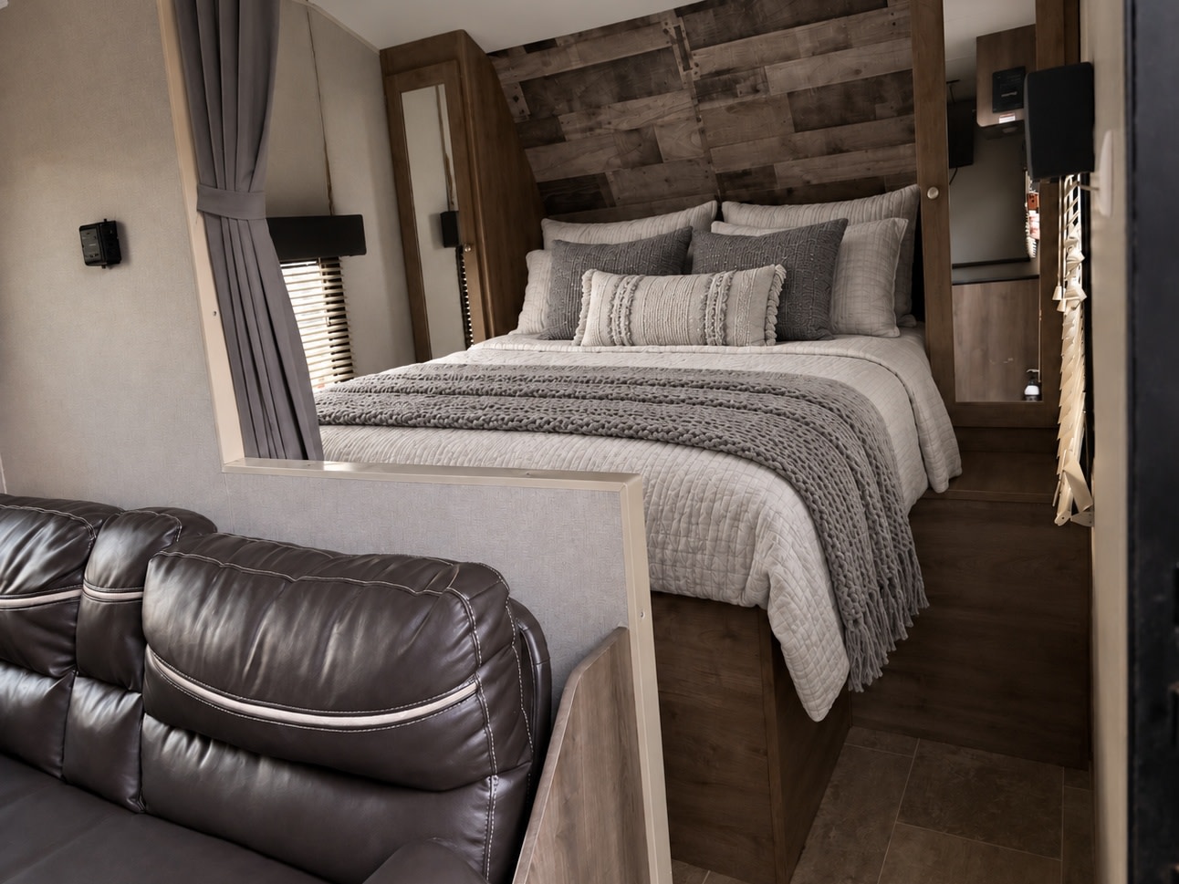 Cozy bedroom in an RV rental, featuring a comfortable bed with gray linens and a brown leather sofa. Perfect for travel comfort.. Aspen Trail LE 2022