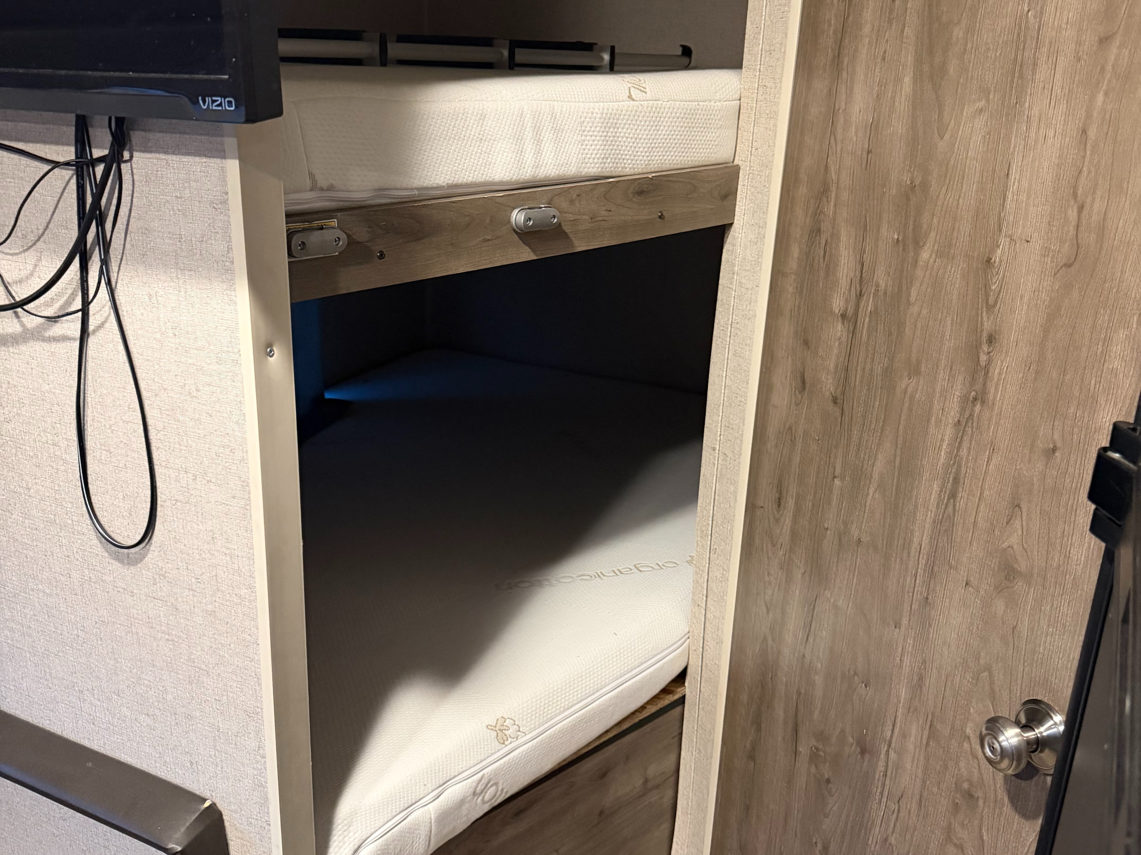Cozy RV rental interior: bunk beds with organic cotton mattresses, a Vizio TV, and a wooden door.. Aspen Trail LE 2022