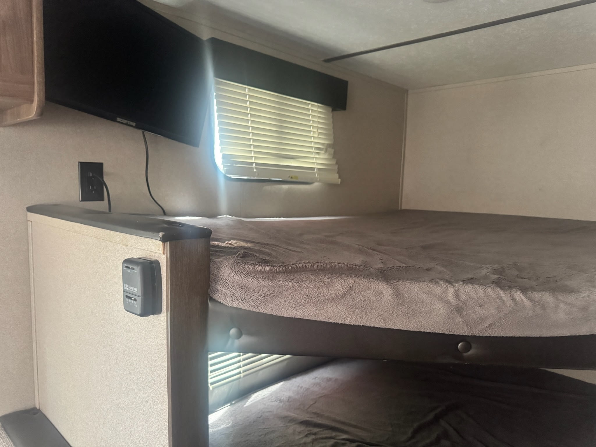 Cozy bunk beds in an RV rental, featuring a TV, window with blinds, and thermostat for comfort. Perfect for family trips.. Keystone RV Hideout LHS 2019