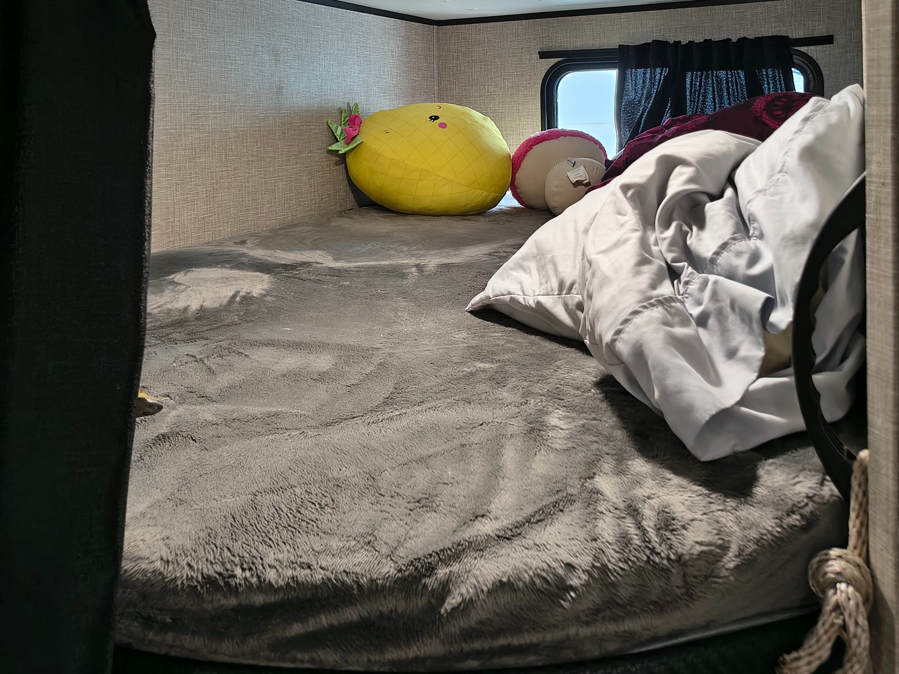 Cozy RV rental bunk bed with soft grey bedding, pineapple & macaron plush toys, and a window, ready for rest.. Jayco Jay Flight 2023