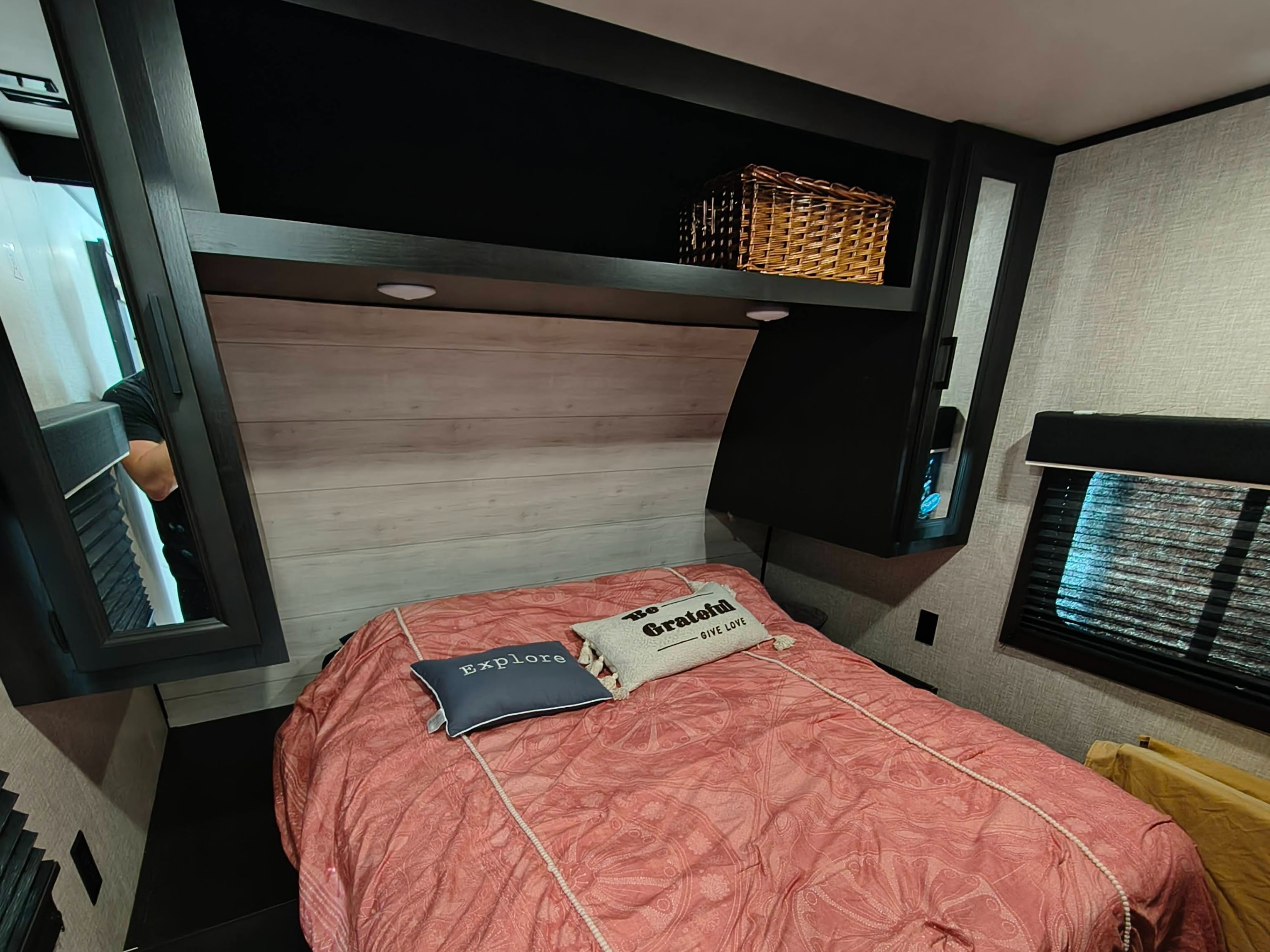 This inviting RV rental bedroom features a pink bed with decorative pillows, overhead storage, and mirrored cabinets.. Jayco Jay Flight 2023