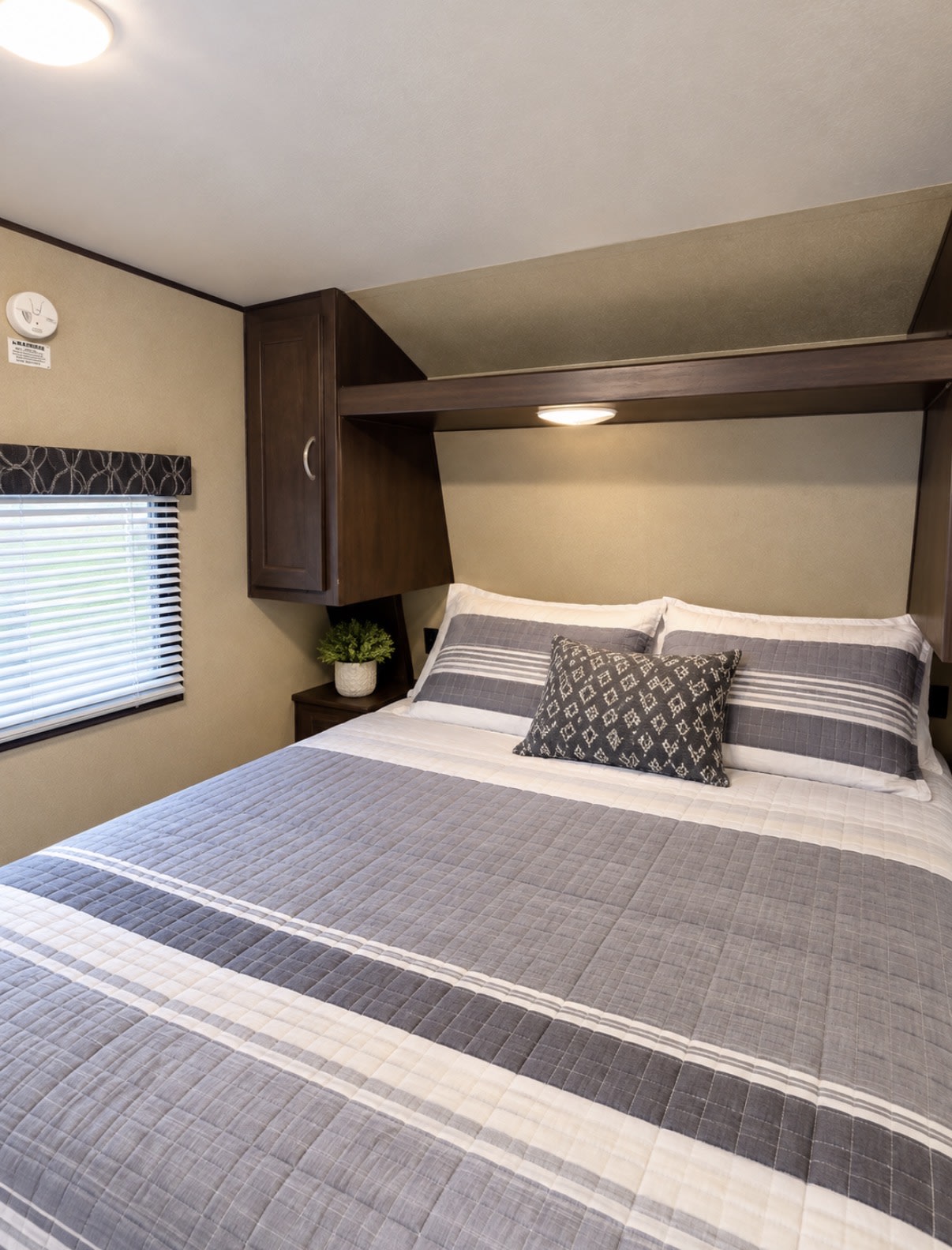 This cozy RV rental bedroom offers a comfortable bed with striped linens and convenient overhead storage.. Keystone RV Springdale SSR 2018