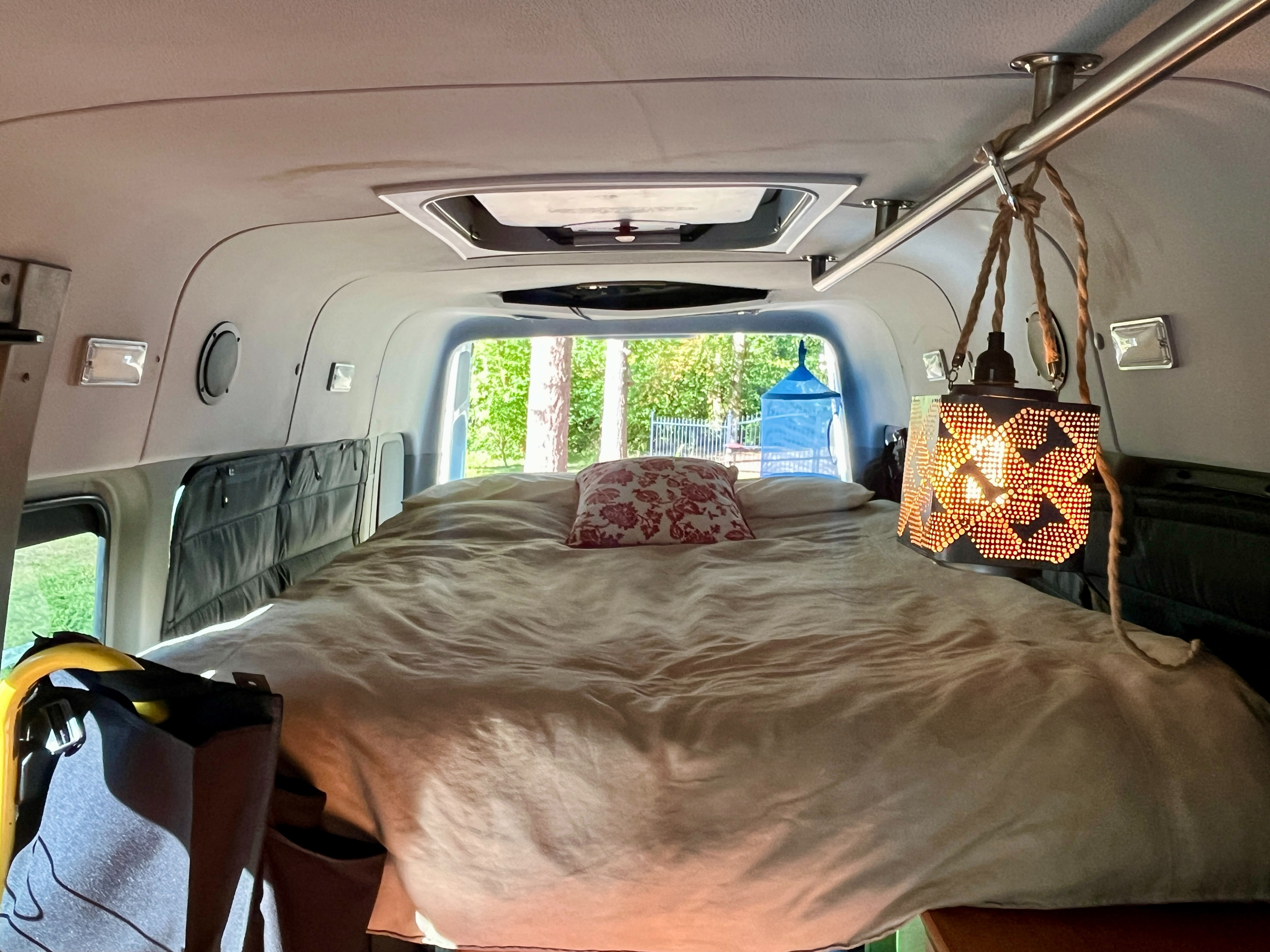 Relax in this cozy rv rental bedroom, featuring a comfy bed, unique lamp, and serene nature views. Perfect for travelers.. Winnebago Mercedes Sprinter 2014