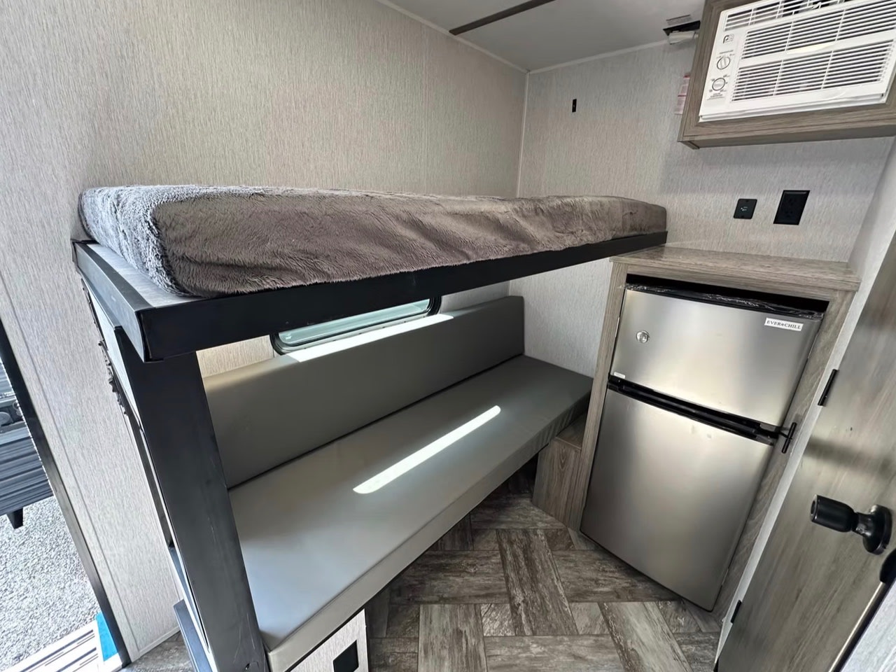 RV rental interior: cozy bunk bed, grey bench seating, mini-fridge, and AC unit. Compact living for adventure.. Sunlite 13BHLTD 2027