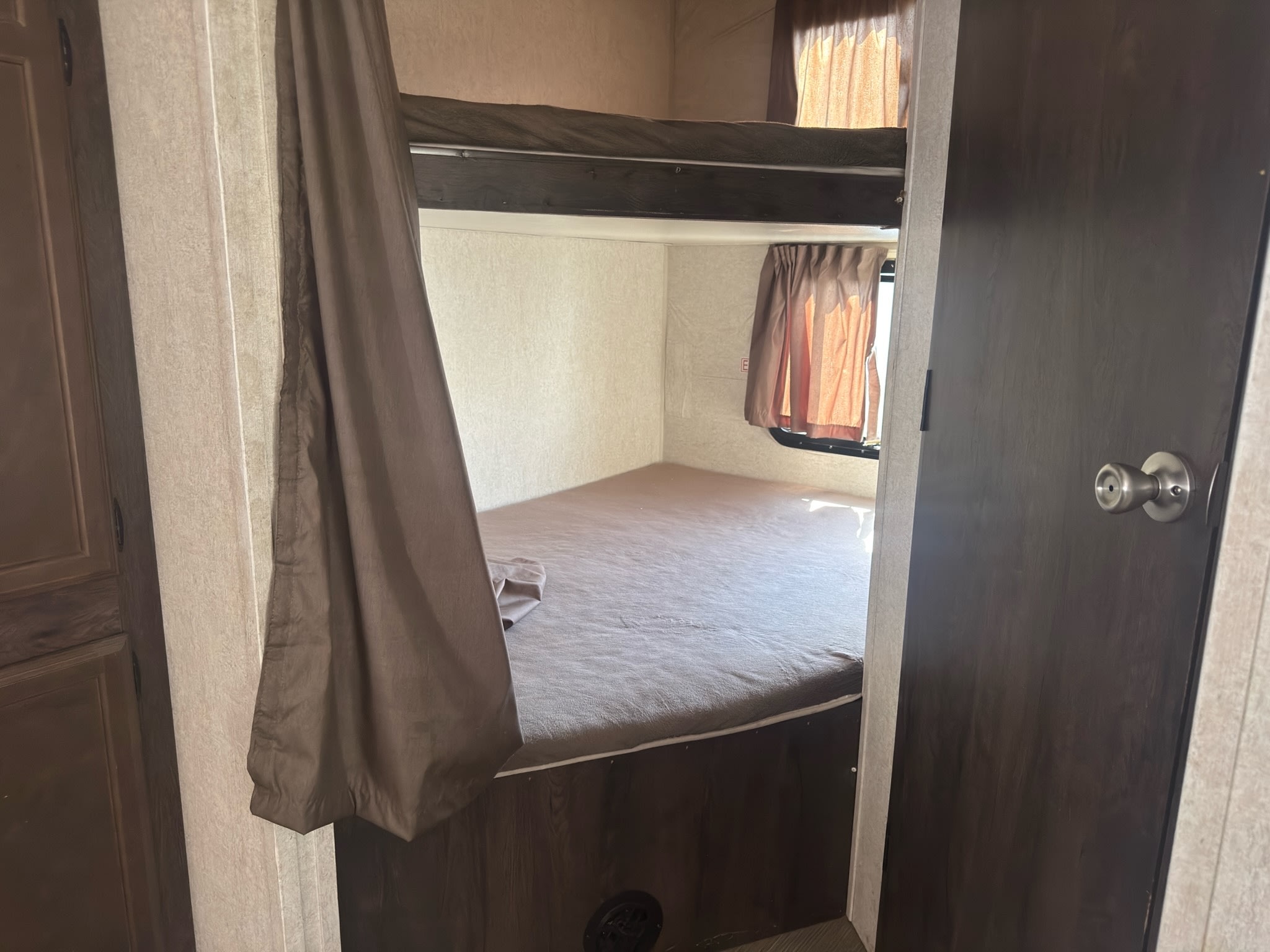 RV rental bunk bed area with a lower mattress, upper bunk, and privacy curtains, seen from a doorway.. Starcraft GPS 2018