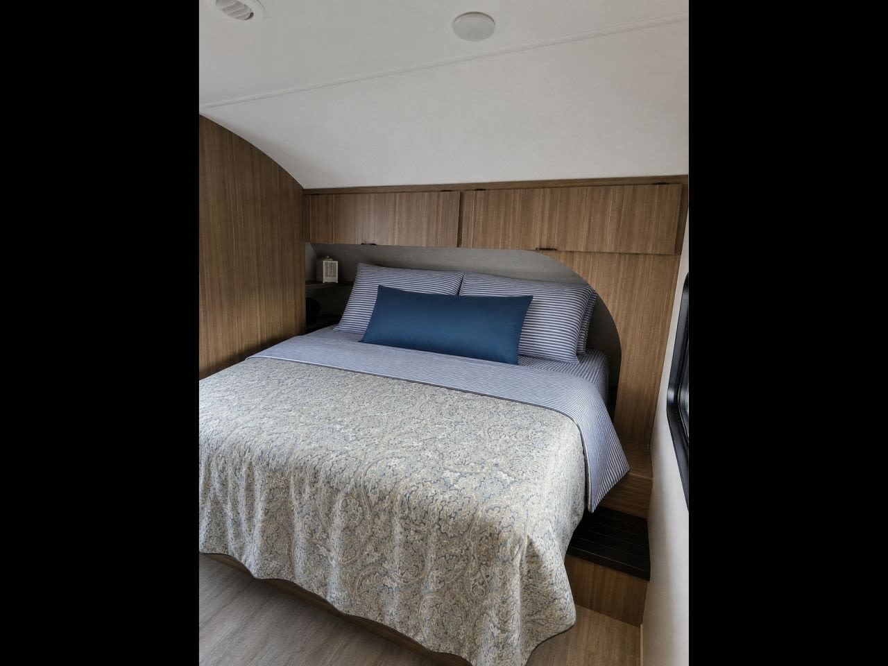 RV rental bedroom: a cozy bed with blue & white bedding and wooden interior, perfect for comfortable travel.. Forest River Wildwood X-Lite 2025