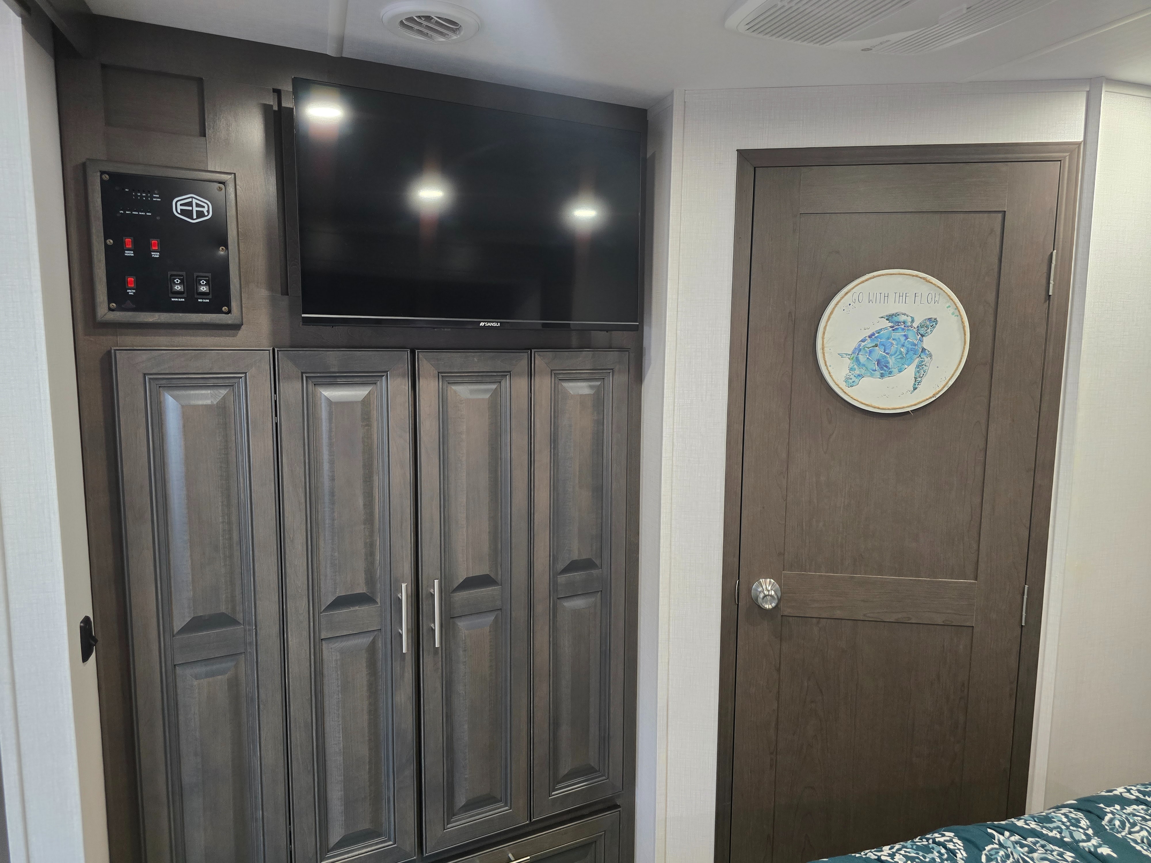 RV rental interior featuring a control panel, Sansui TV, dark wood cabinets, and a door with a turtle "Go With The Flow" sign.. Georgetown GT3 2026
