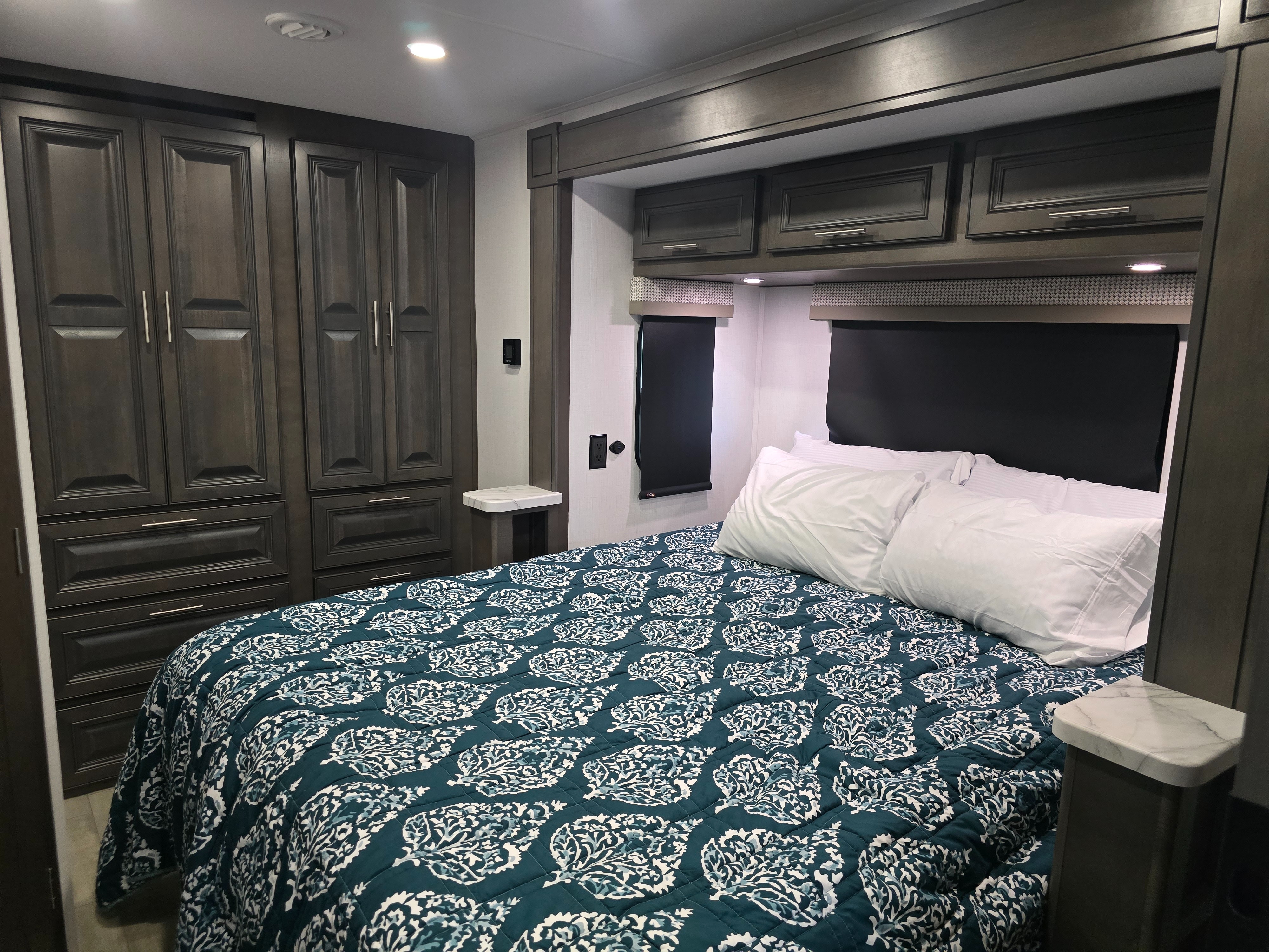 Spacious RV rental bedroom with dark wood cabinets, a teal patterned comforter, and comfortable pillows for your journey.. Georgetown GT3 2026